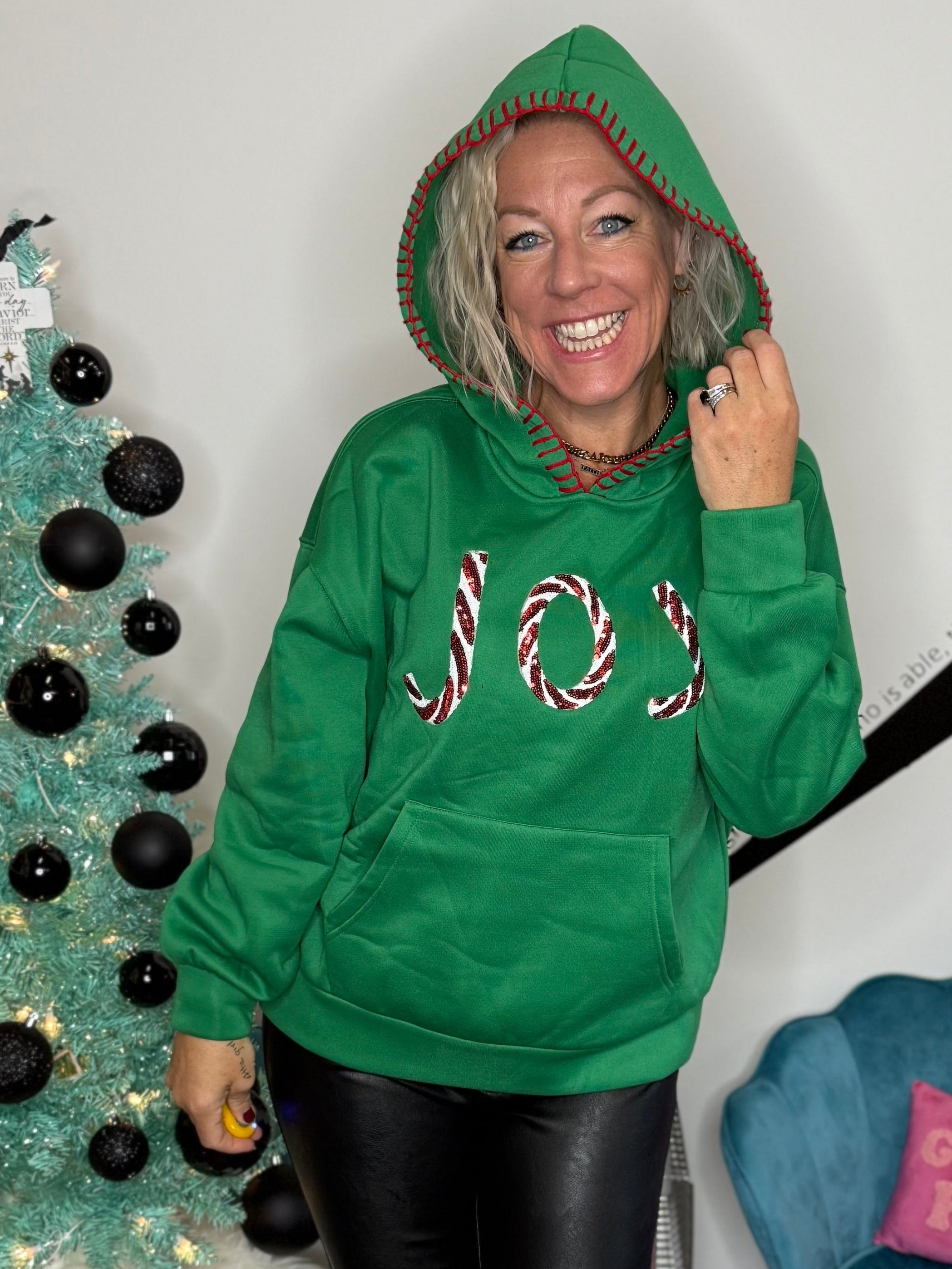 Person wearing a green hoodie with candy cane design in a room with a decorated Christmas tree and blue chair.