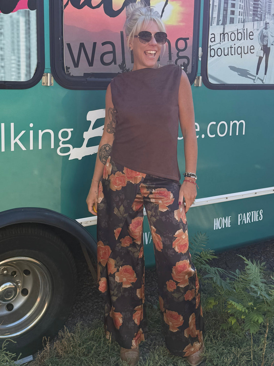 A woman stands in front of a teal mobile boutique bus with the text &