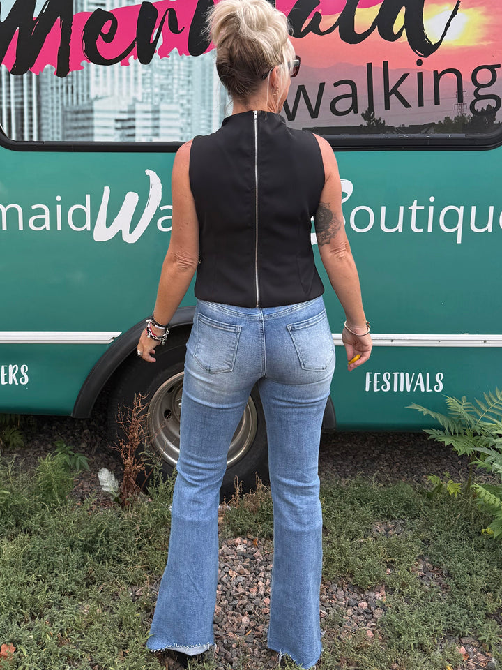 A woman stands with her back to the camera in front of a teal bus printed with &