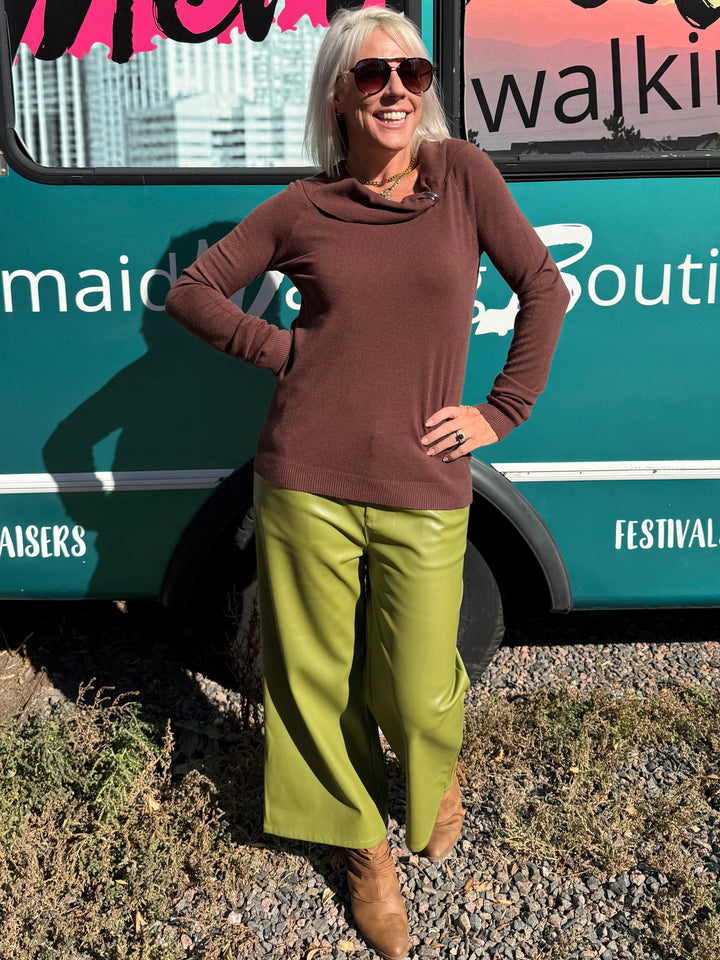 A woman stands in front of a teal bus with &