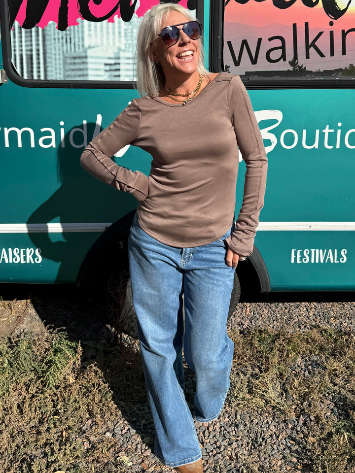 A woman with blonde hair and sunglasses stands in front of a teal bus with &