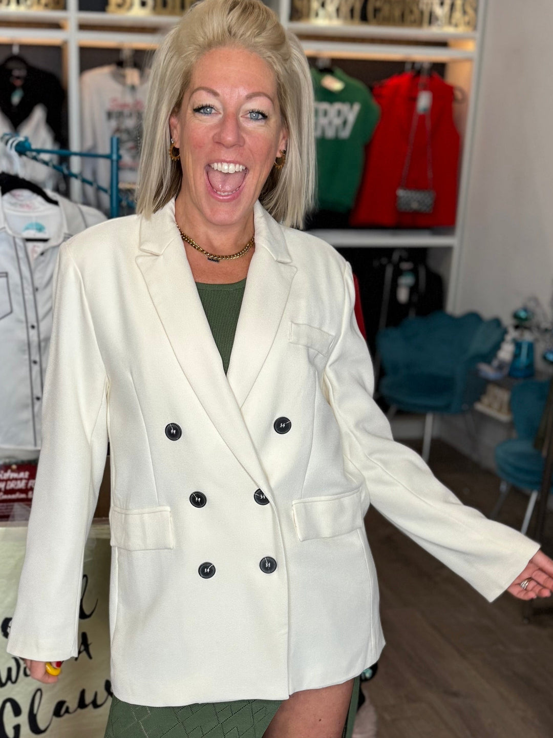 Woman in a white blazer and green skirt standing in a clothing store.