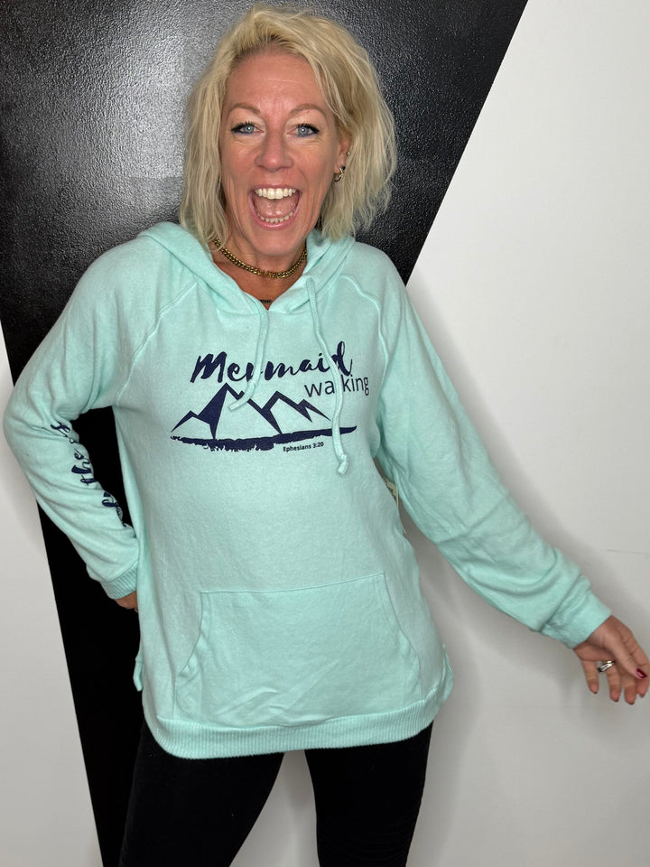 Person wearing a light blue hoodie with a logo on a black and white floor.