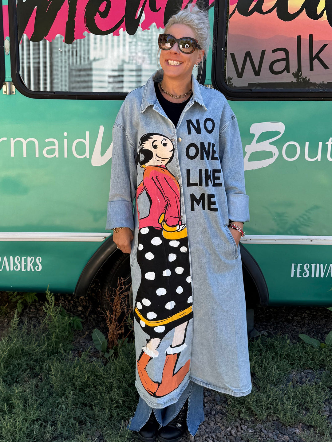 A woman stands in front of a turquoise bus with &