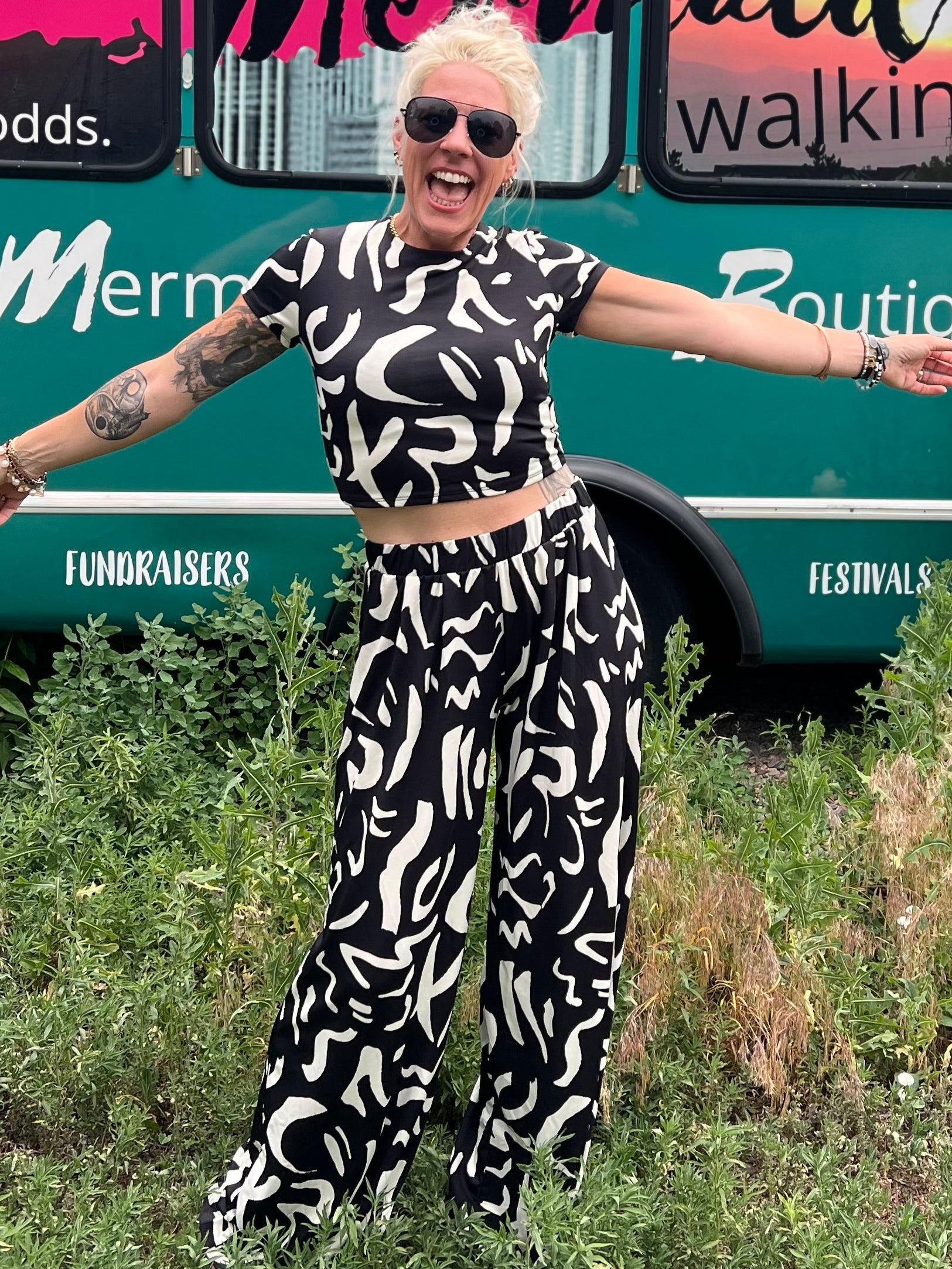 Person wearing a black and white patterned outfit standing outdoors with a bus in the background.