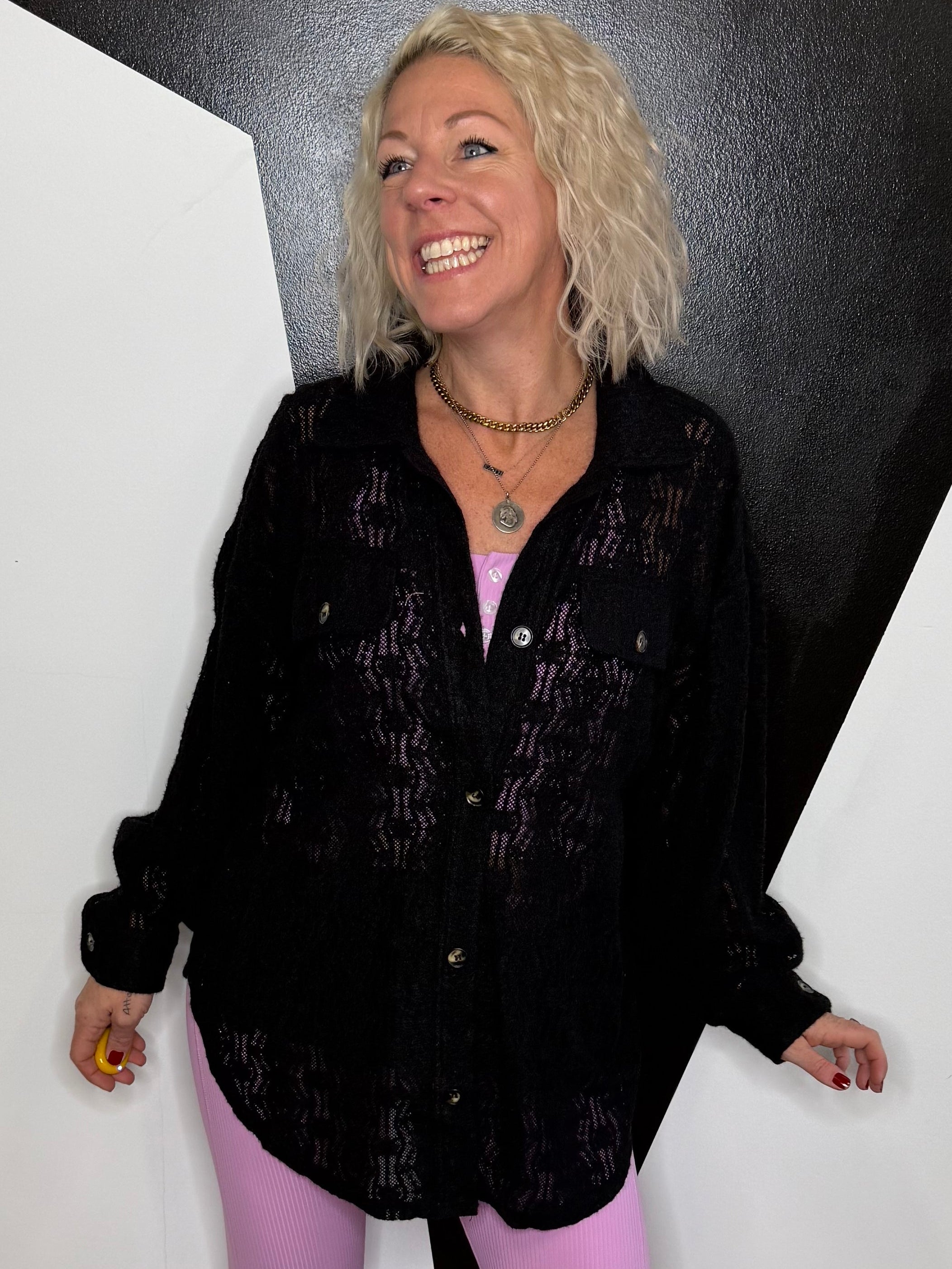 Person wearing a black lace button up top in front of geometric background.