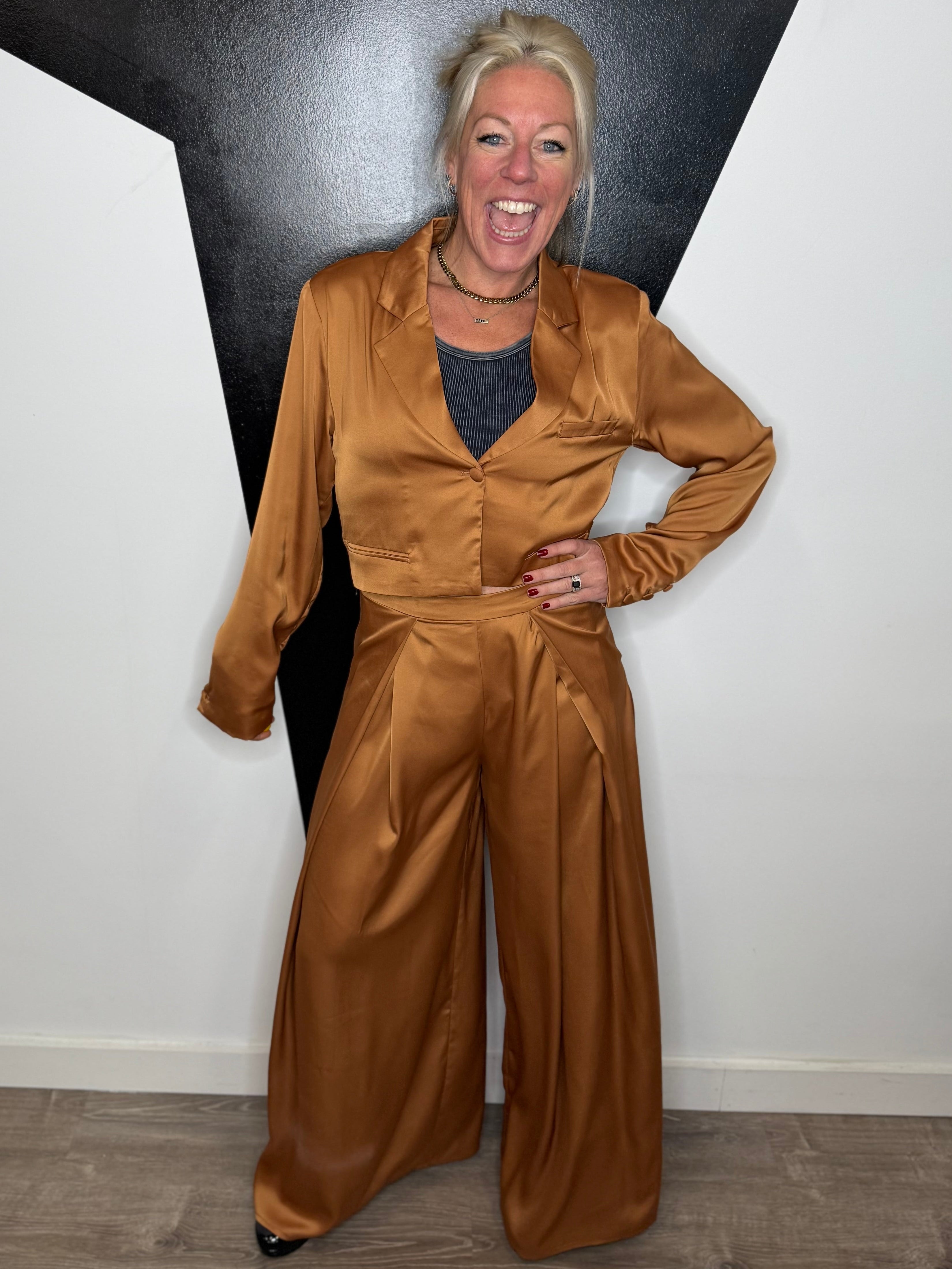 Person wearing a brown satin suit standing against a black and white geometric wall.