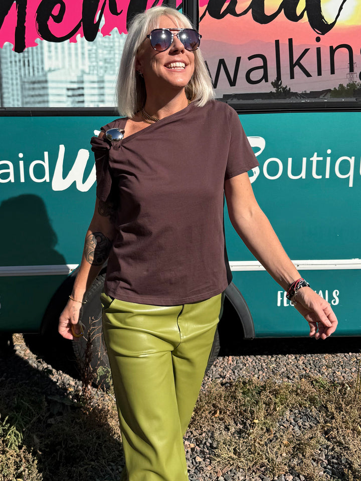 A woman stands outdoors in front of a teal bus with &