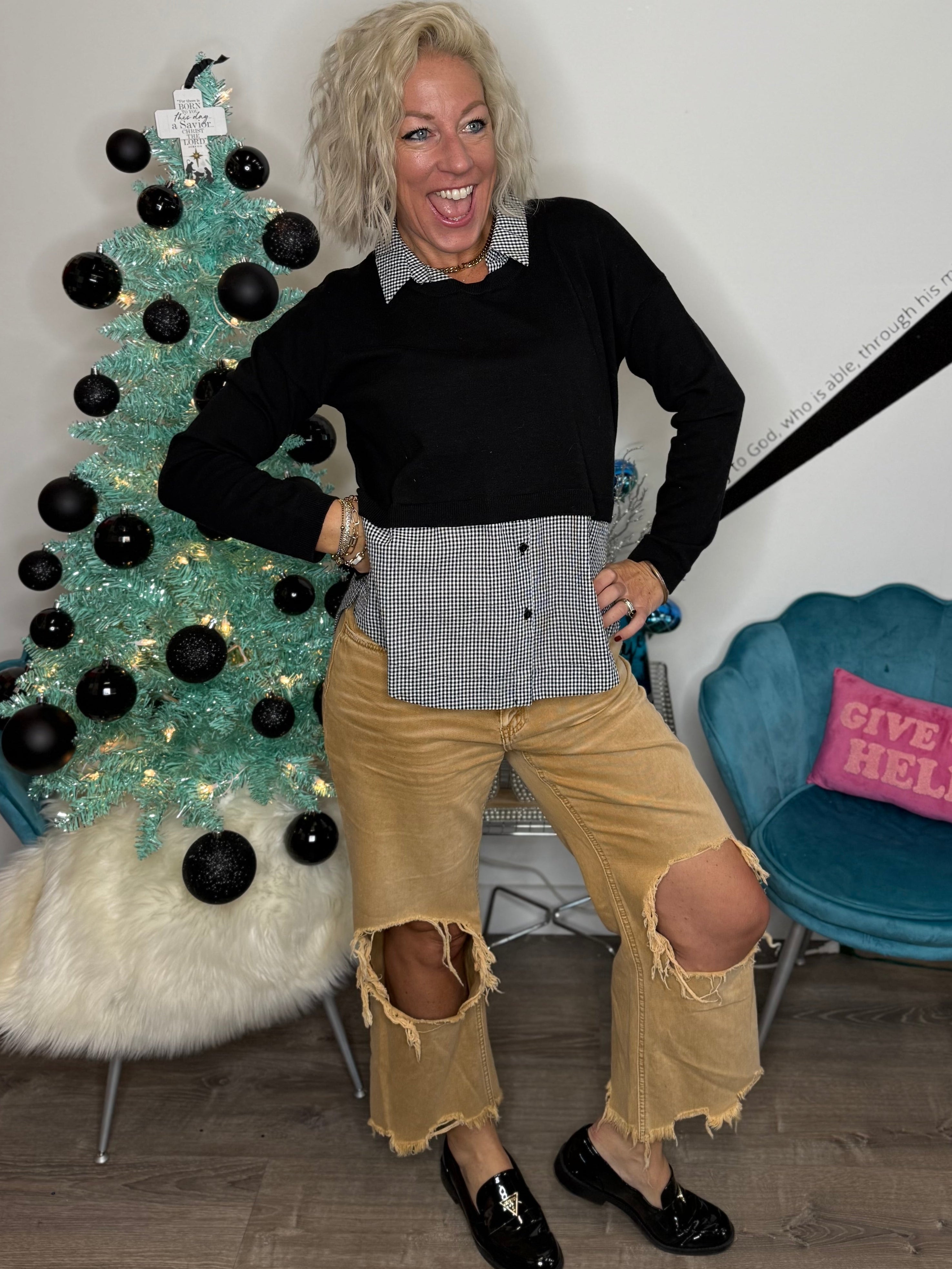 Woman posing in front of a decorated Christmas tree with a blue chair and pink pillow in the background.
