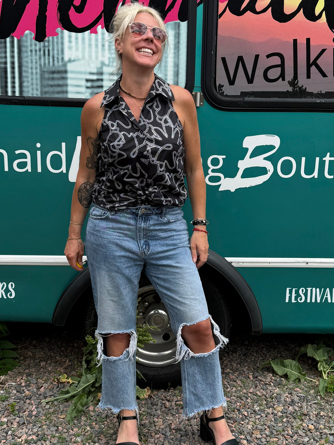 A woman stands in front of a teal mobile boutique bus with &