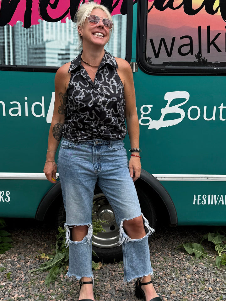 A woman stands in front of a teal mobile boutique bus with &