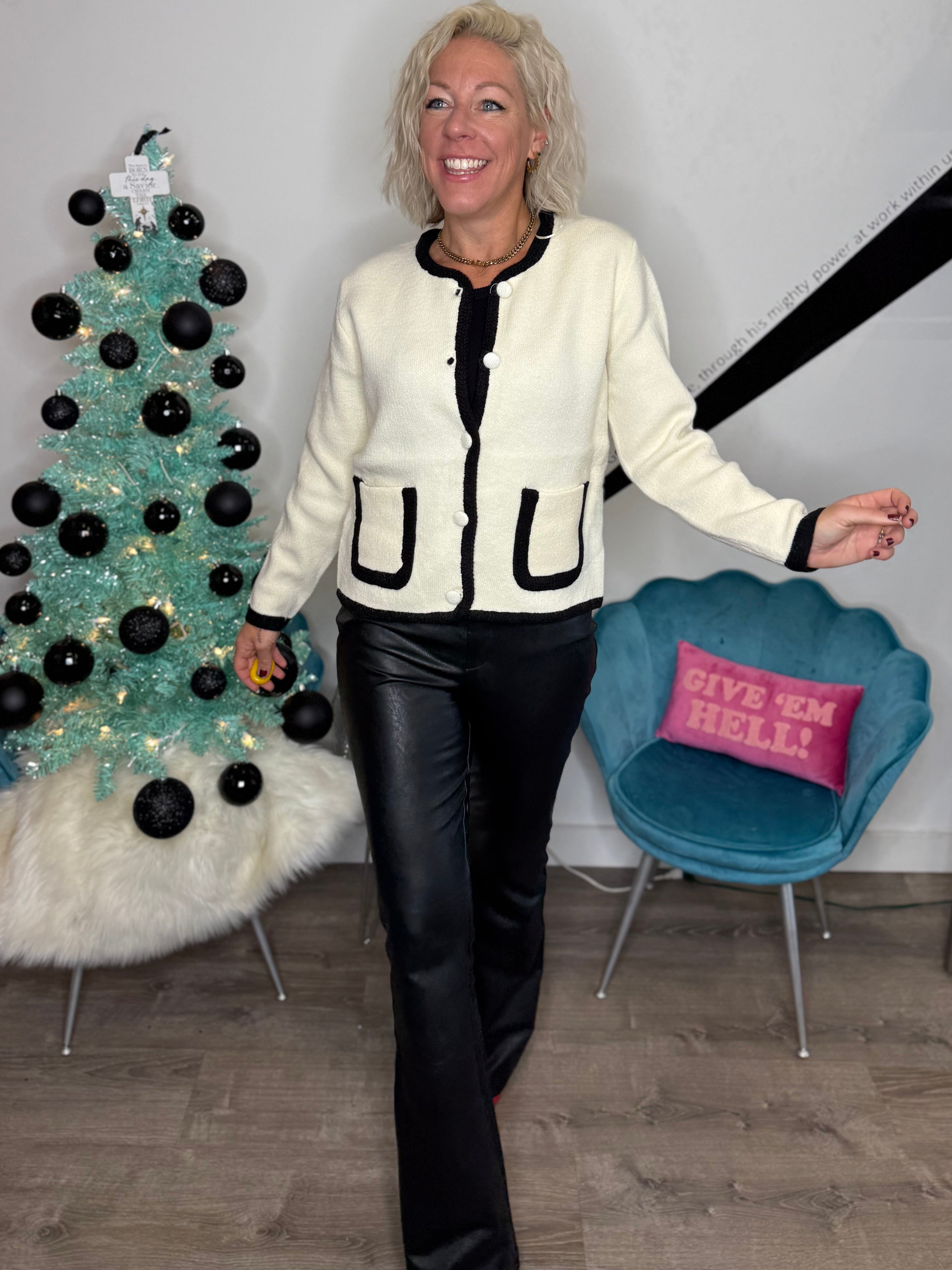 Woman standing in a room with a decorated Christmas tree and a blue chair with a pink pillow.