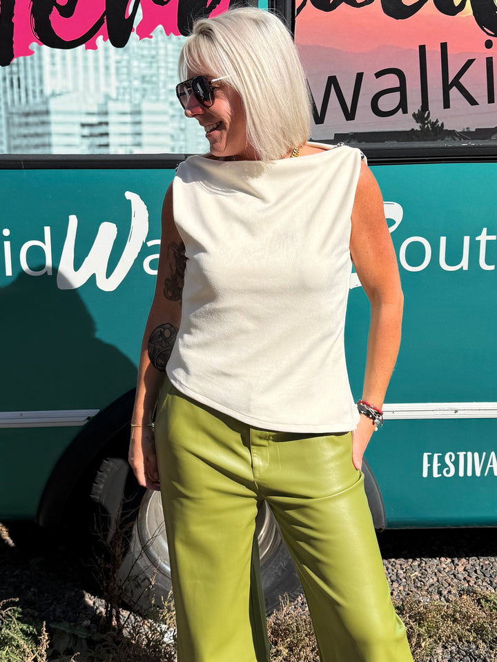 A woman with short blonde hair and sunglasses stands in front of a teal bus with &