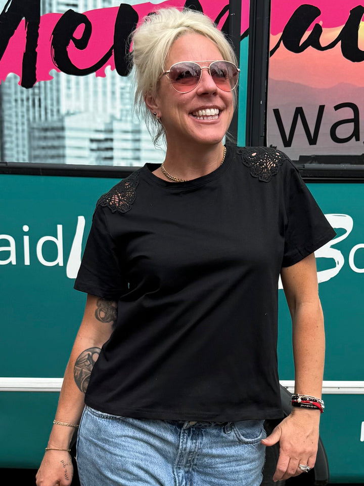 A woman with blonde hair and sunglasses stands in front of a teal bus with &