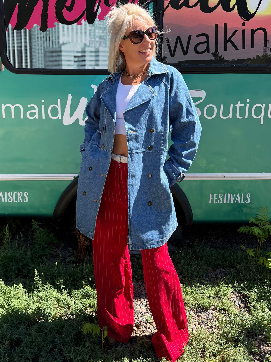 A woman stands outdoors in front of a teal bus with &