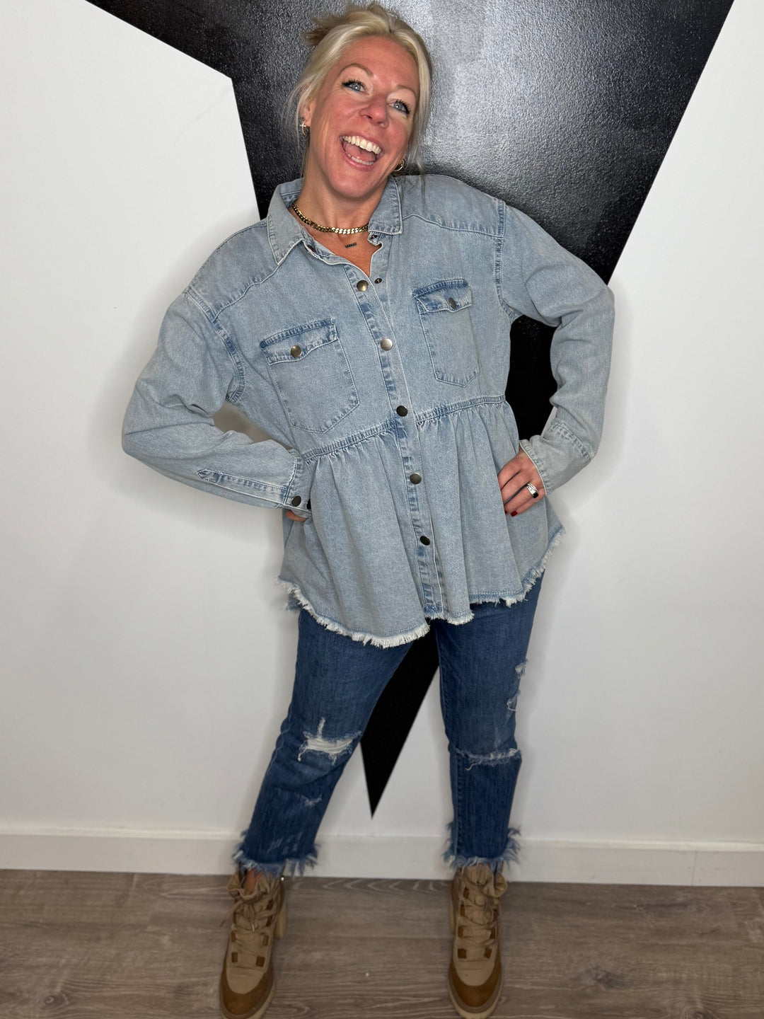 Person wearing a denim jacket and jeans standing against a black and white wall.