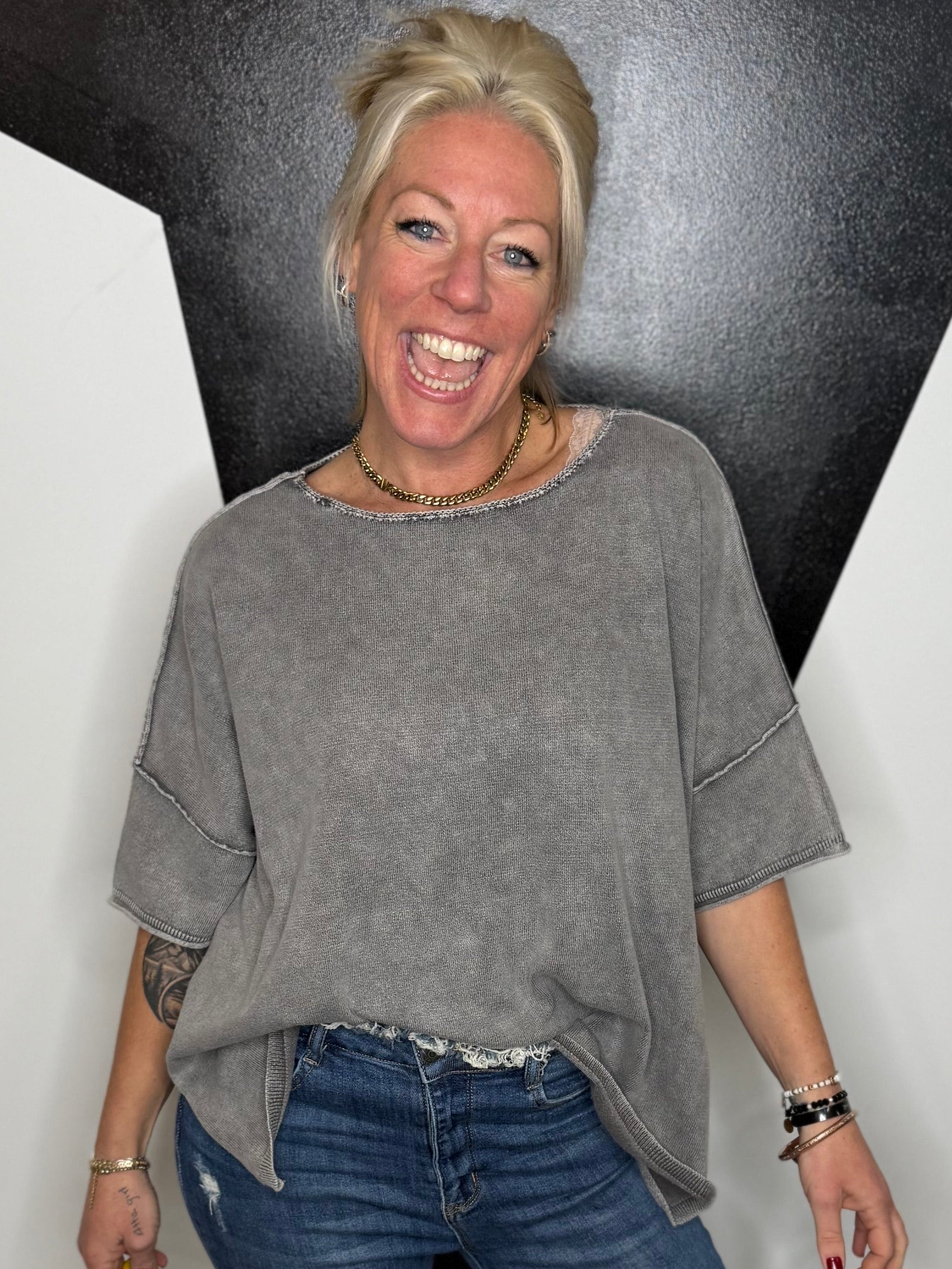 Woman wearing a gray oversized shirt and blue jeans standing against a black and white geometric wall.