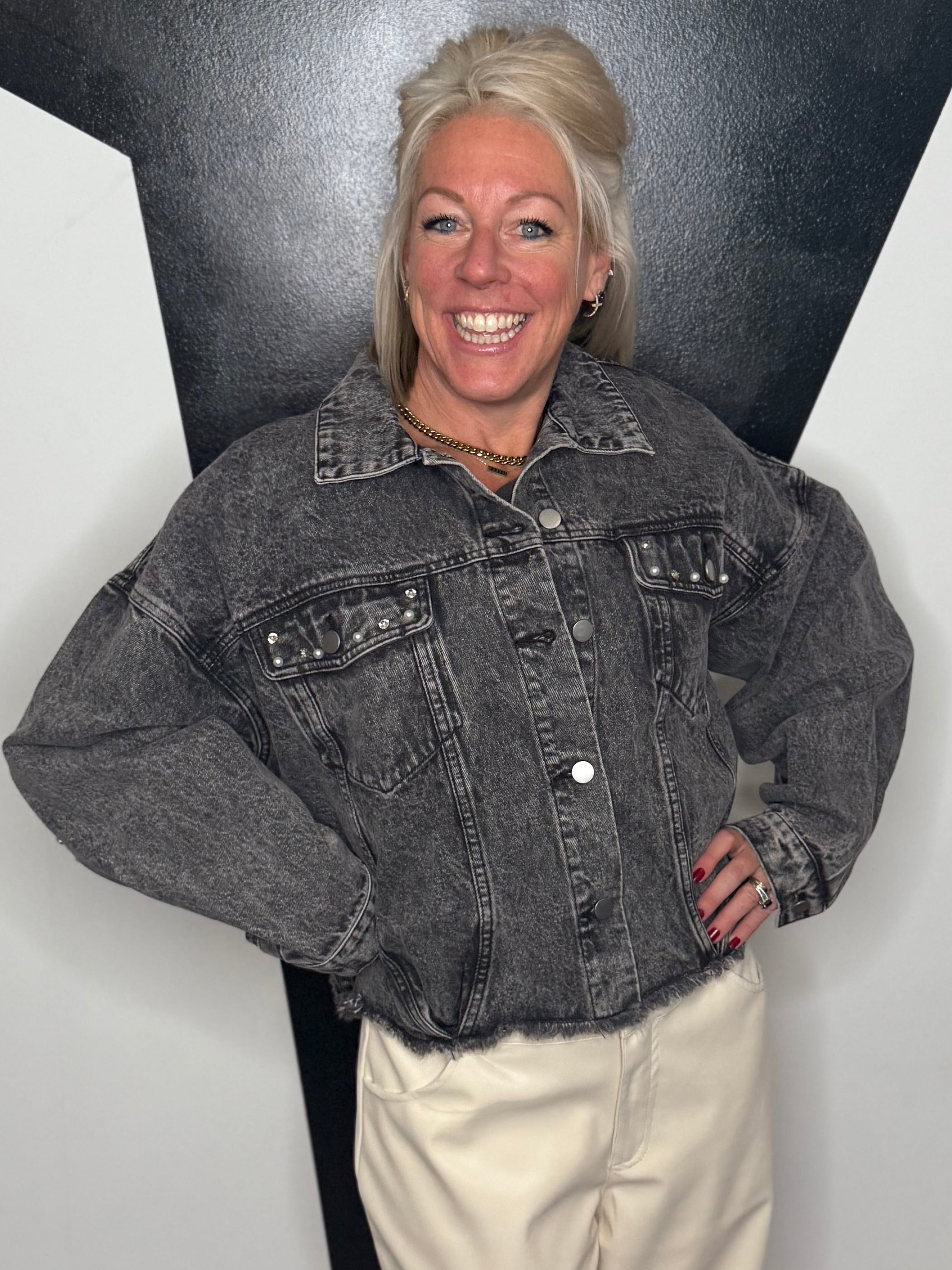Person wearing a denim jacket and beige pants standing against a black and white geometric wall.