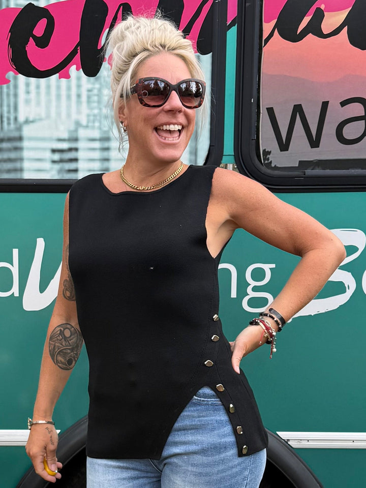 A woman stands in front of a teal bus with large &