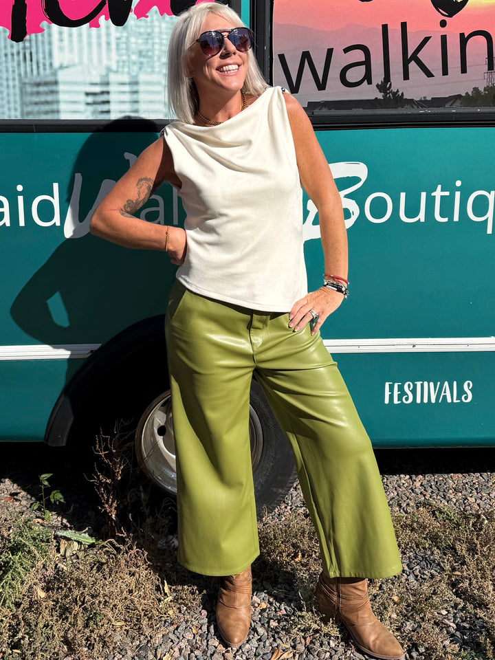 A woman with white hair and sunglasses stands in front of a teal bus with &
