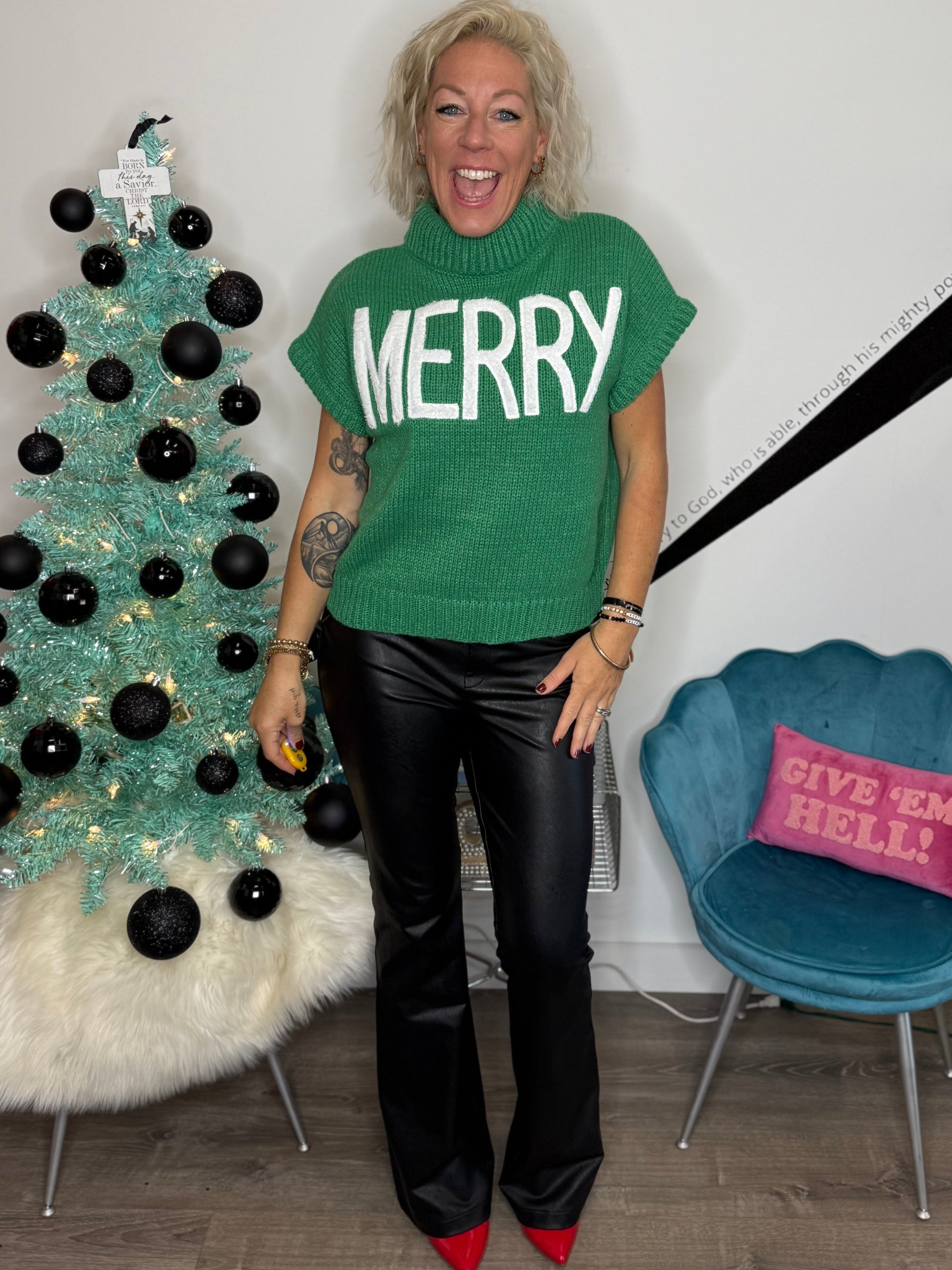 Person wearing a green 'MERRY' shirt standing next to a decorated Christmas tree.