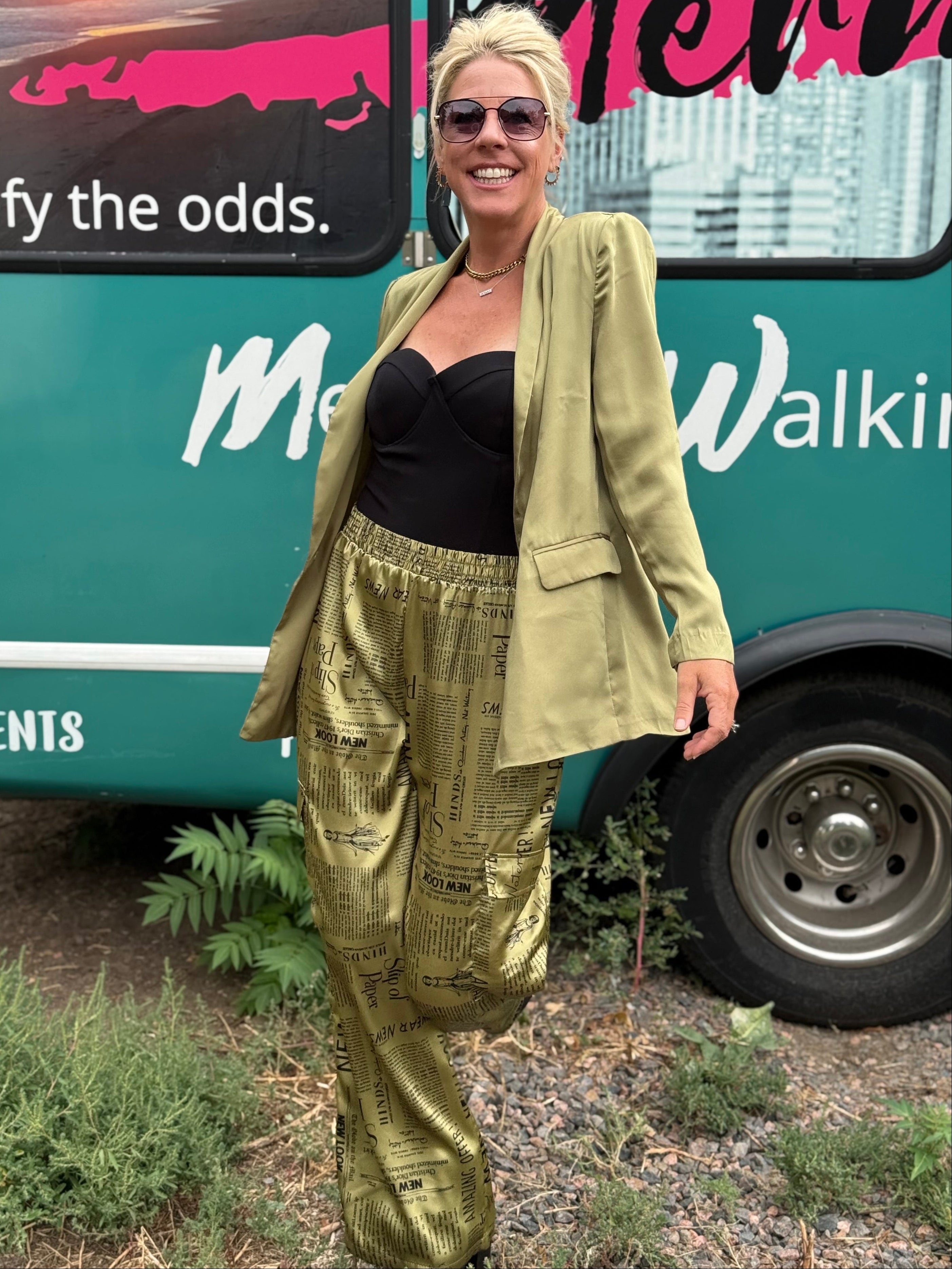 Woman standing in front of a green bus with text, wearing a green jacket and black top.