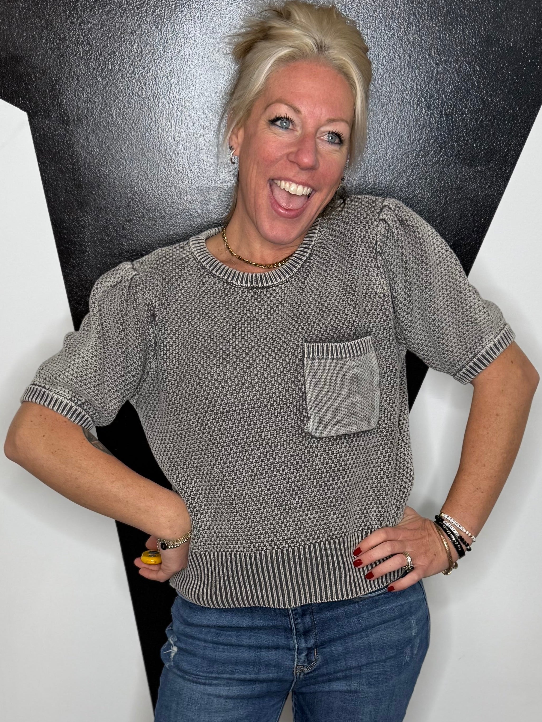 Person wearing a gray sweater and blue jeans standing against a black and white geometric wall.