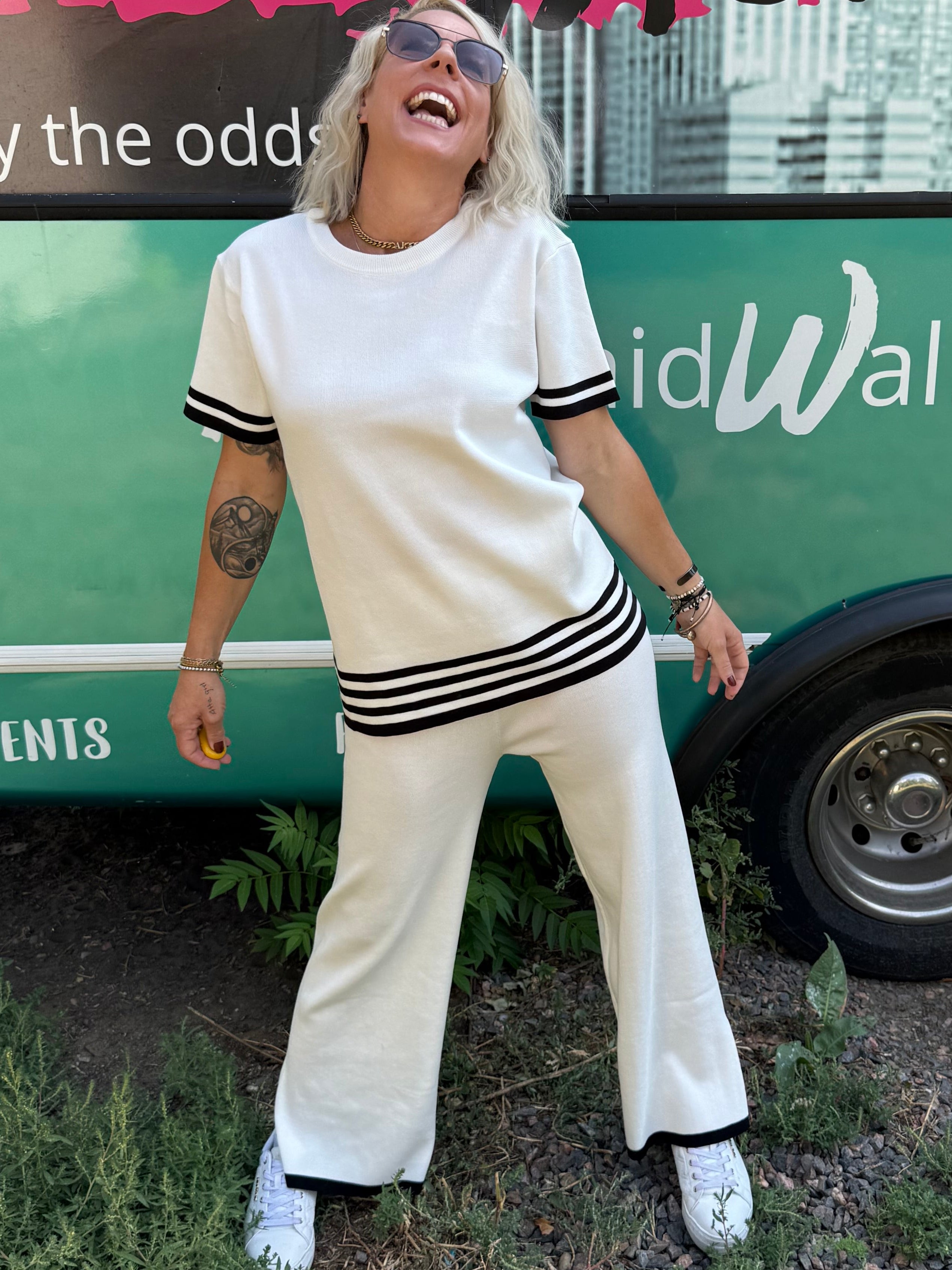 Person in a white outfit standing next to a colorful bus with text on a natural background