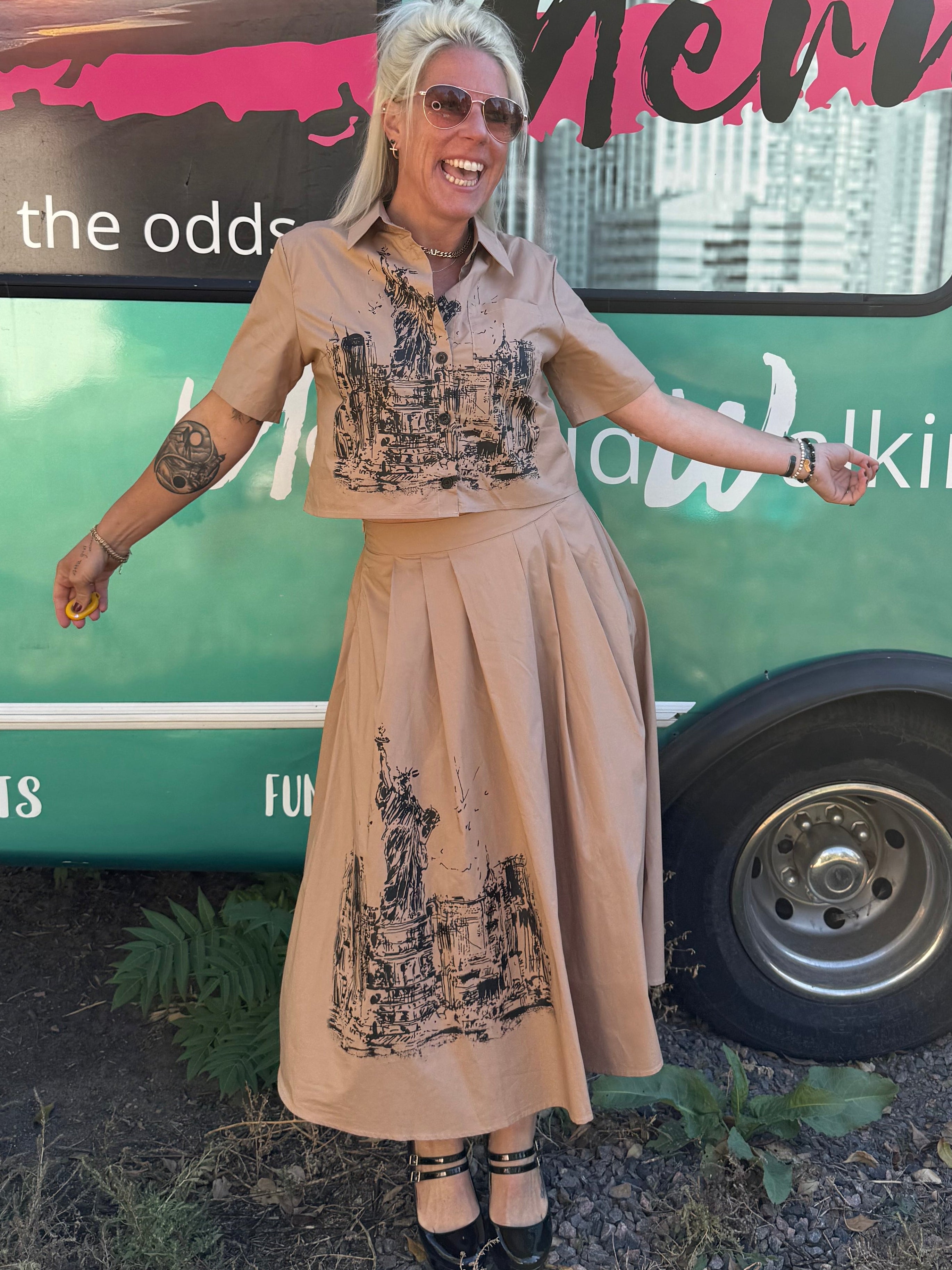 Woman in a beige dress standing next to a green bus with text on the side.