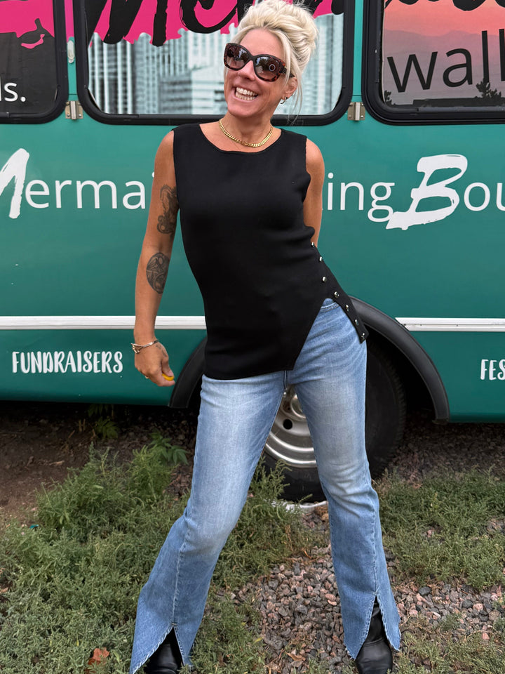 A woman with short blonde hair and sunglasses poses in front of a teal event bus with &