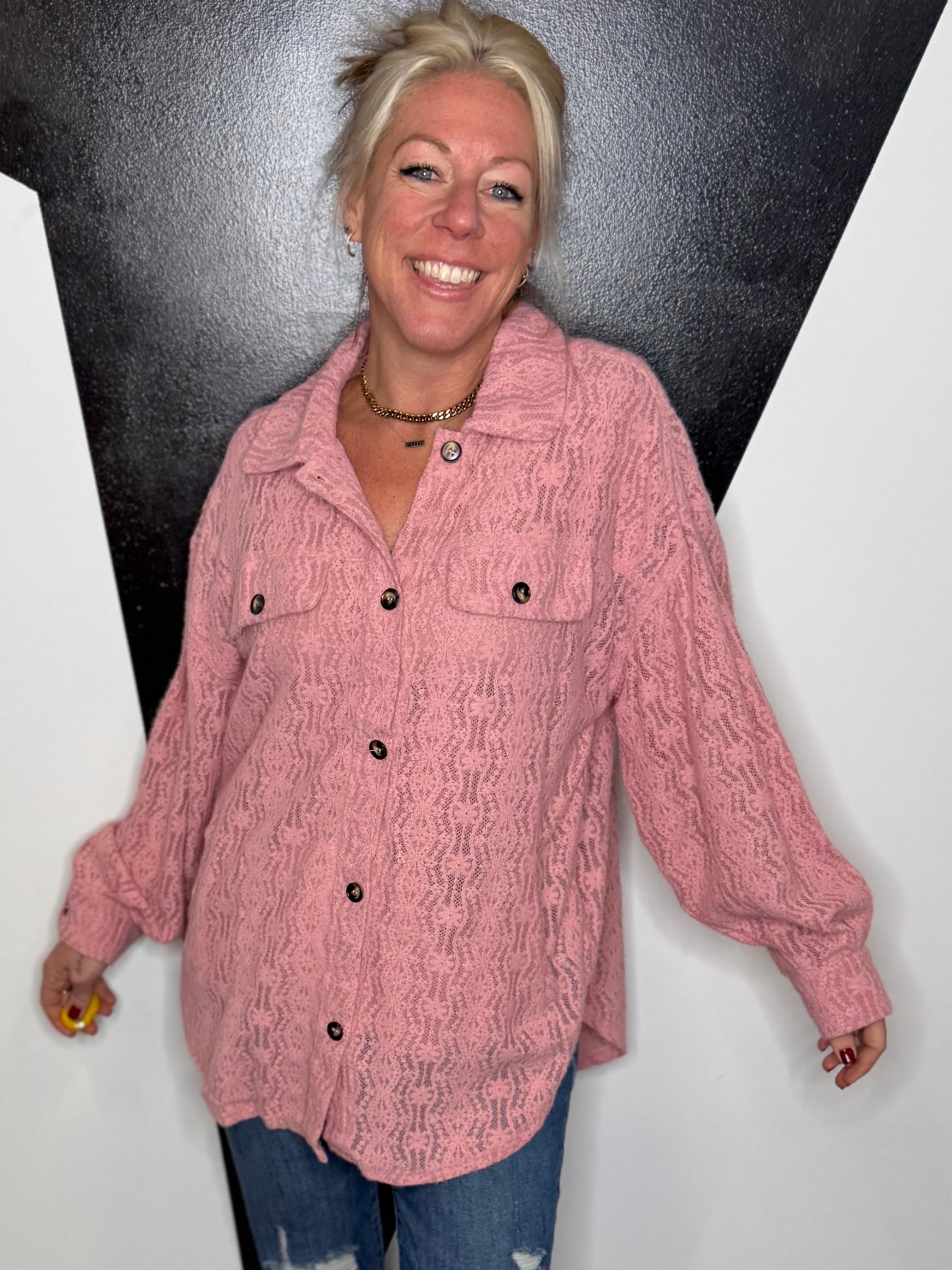 Person wearing a pink jacket and blue jeans standing against a black and white wall.