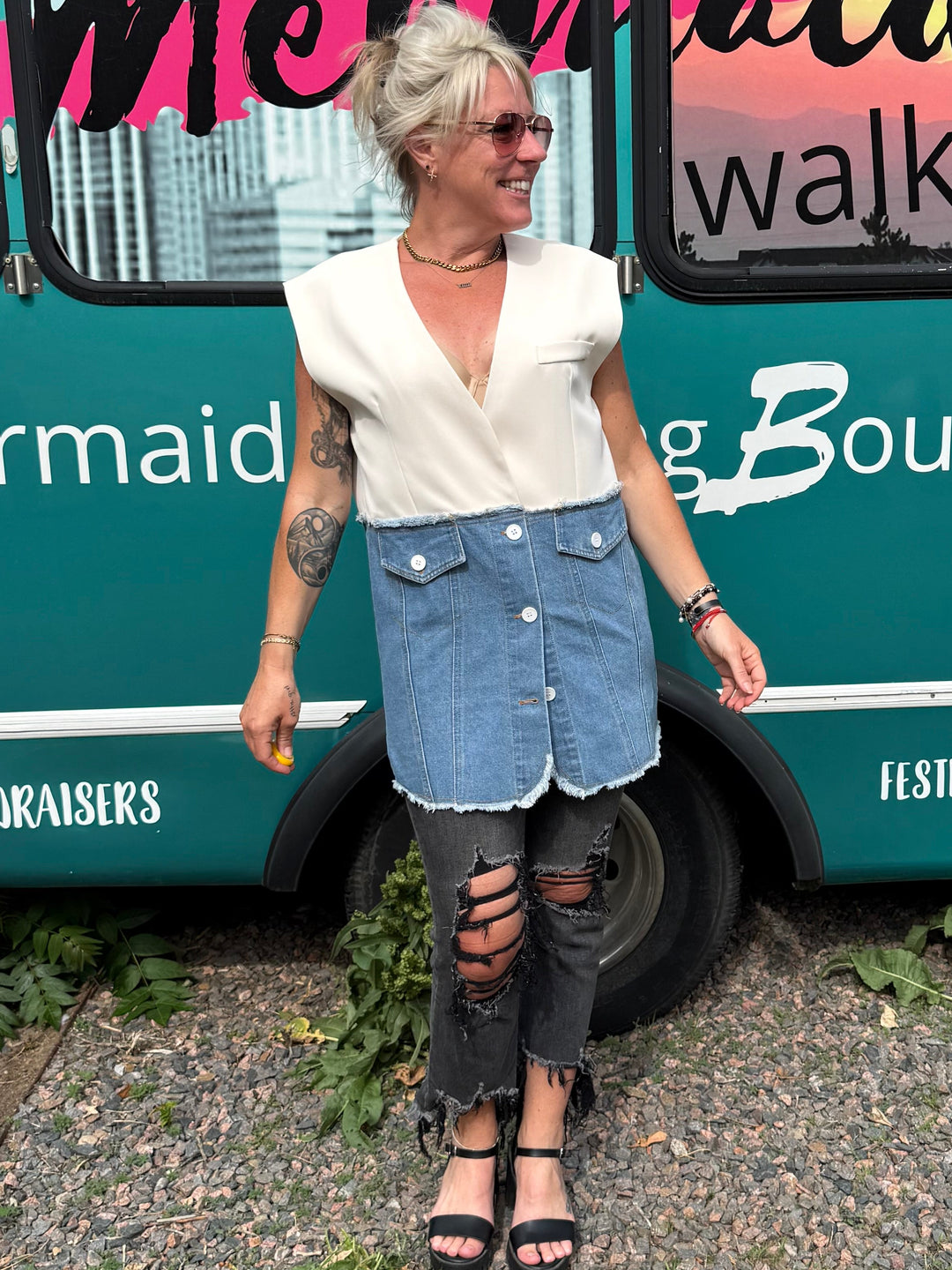 A woman stands in front of a teal bus with &
