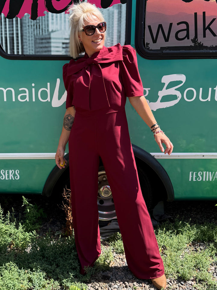 A woman with blonde hair and sunglasses stands in front of a teal bus with &