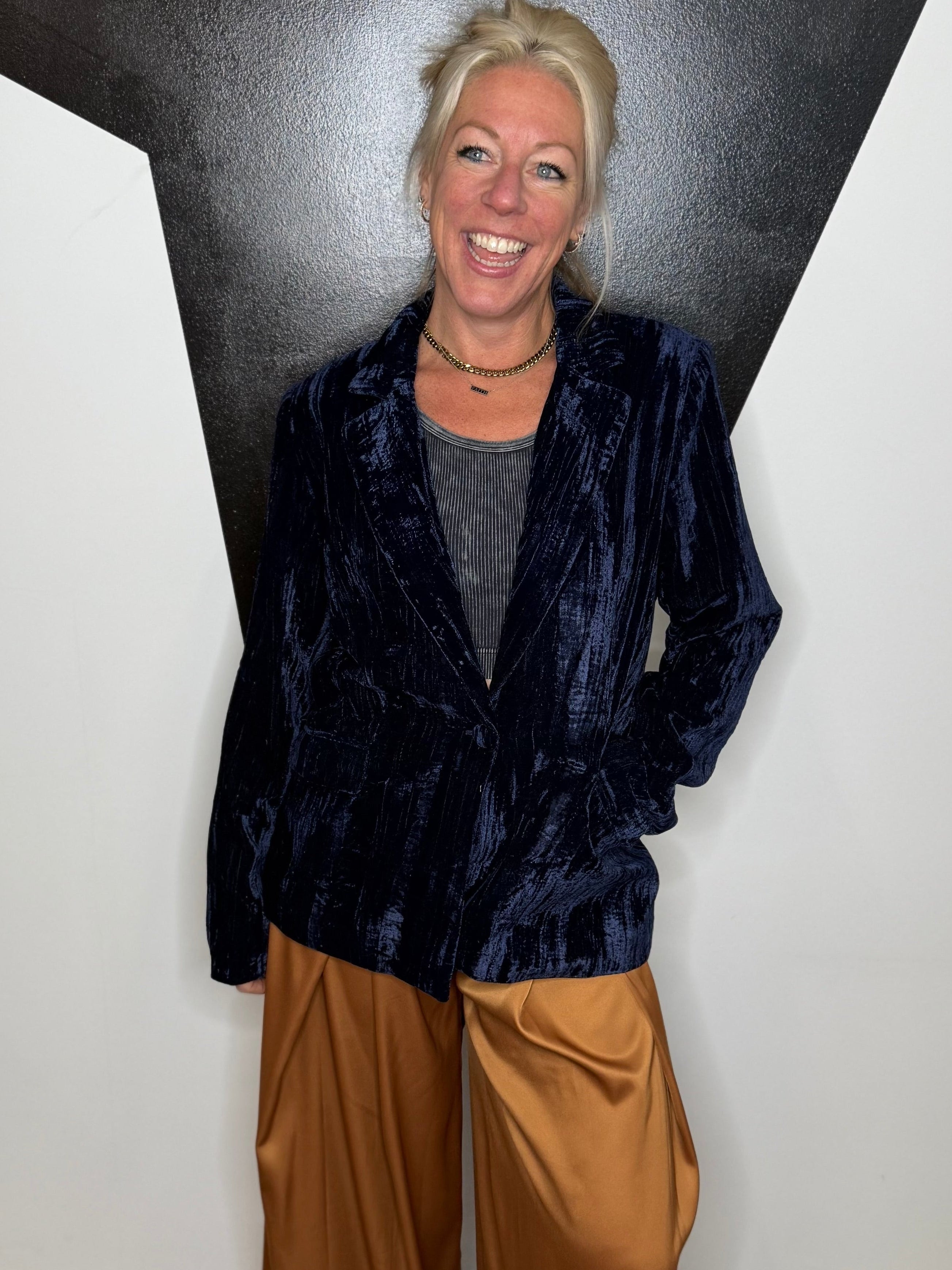 Person wearing a dark blue jacket and brown pants standing against a black and white wall.