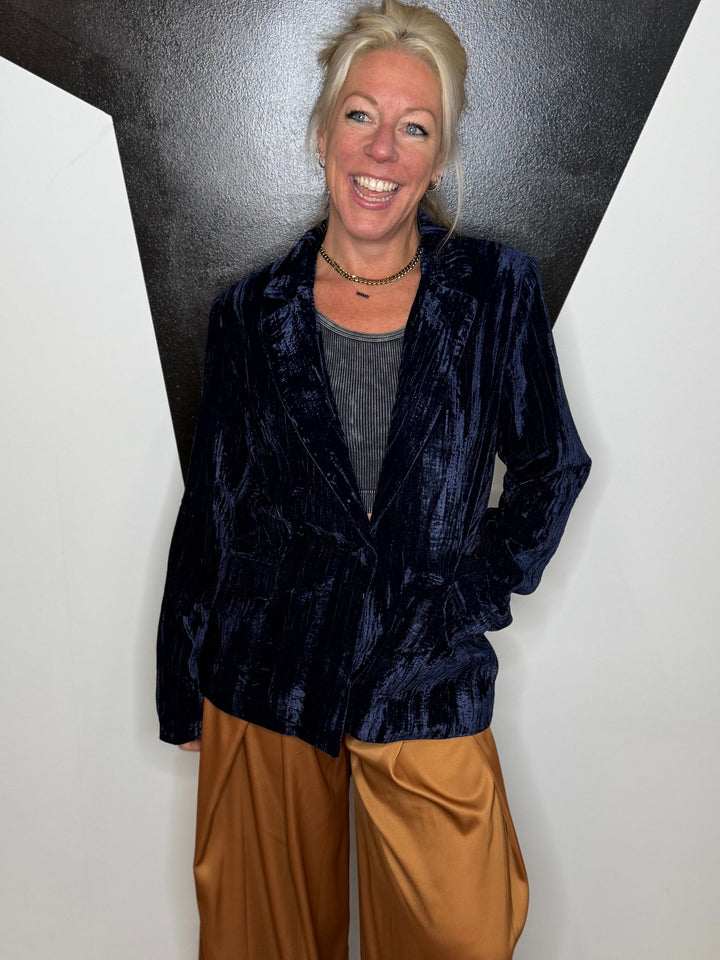 Person wearing a dark blue jacket and brown pants standing against a black and white wall.