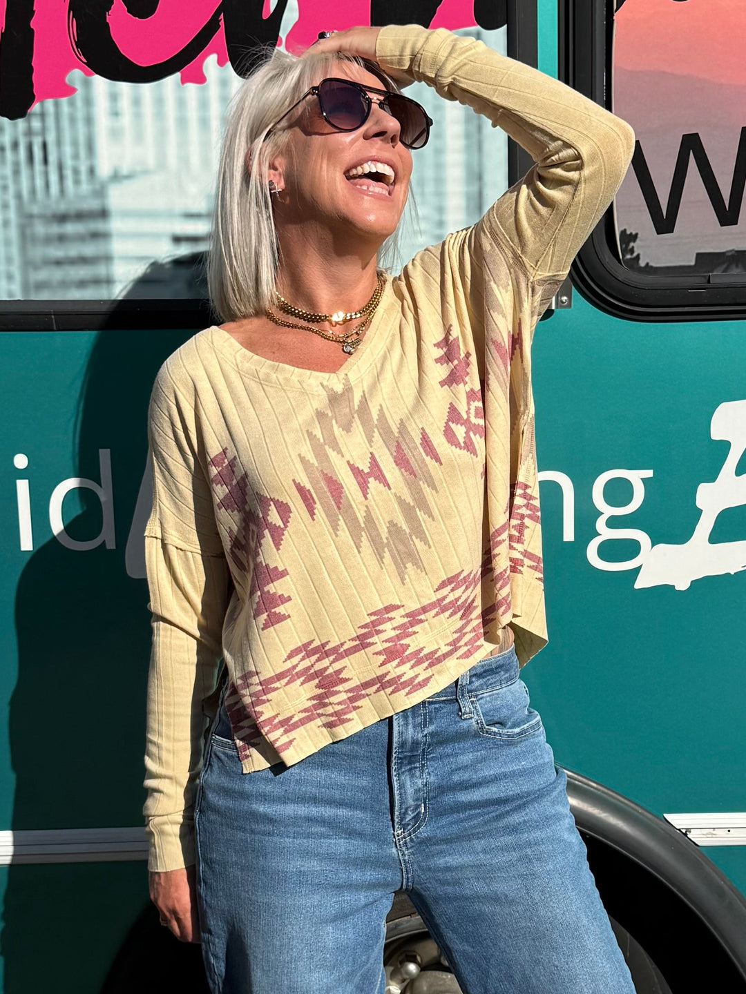 A woman posing outdoors in front of a teal bus with &