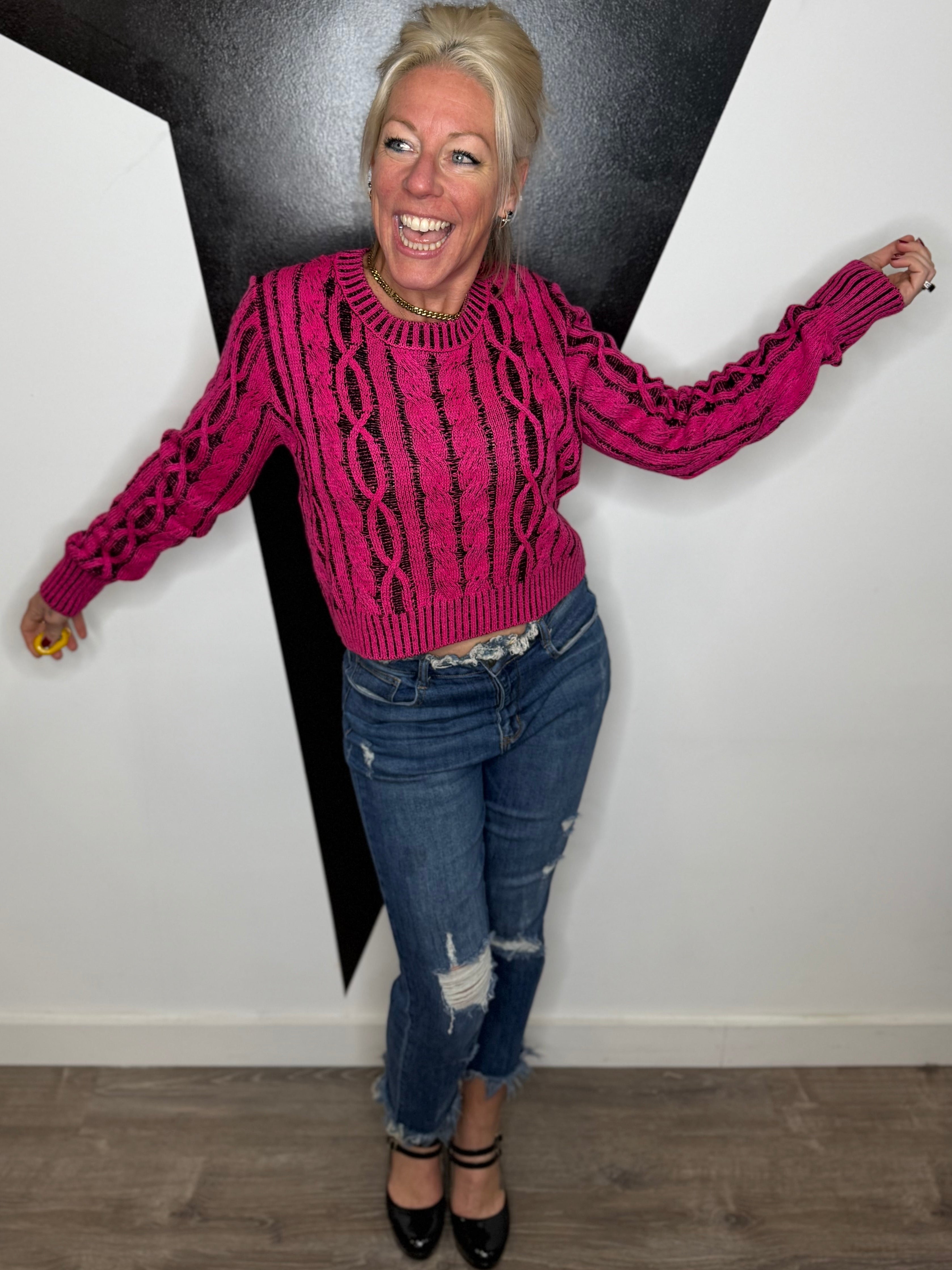 Person wearing a pink sweater and blue jeans standing in front of a black and white wall.