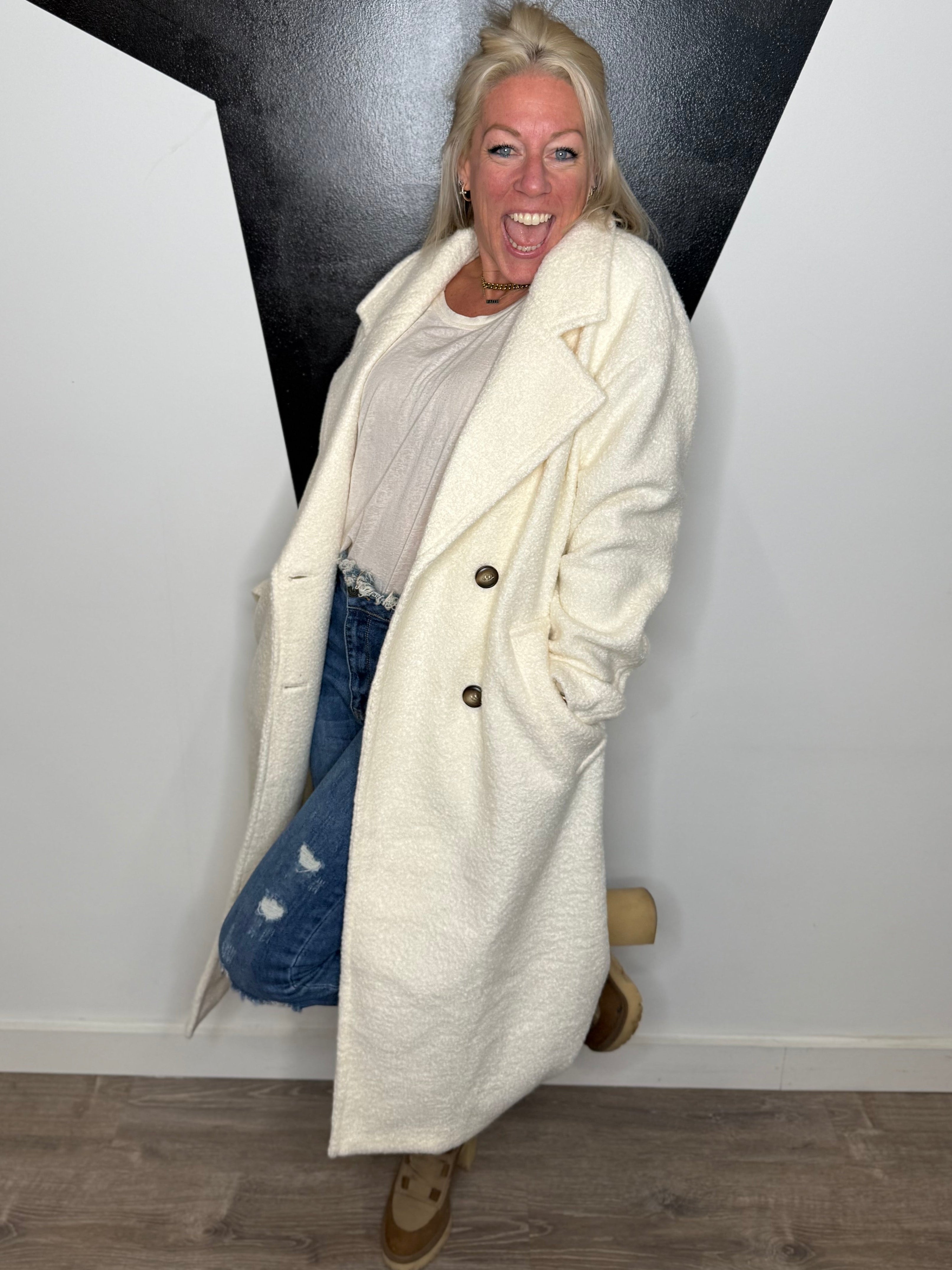Person wearing a long cream coat standing against a black and white wall.