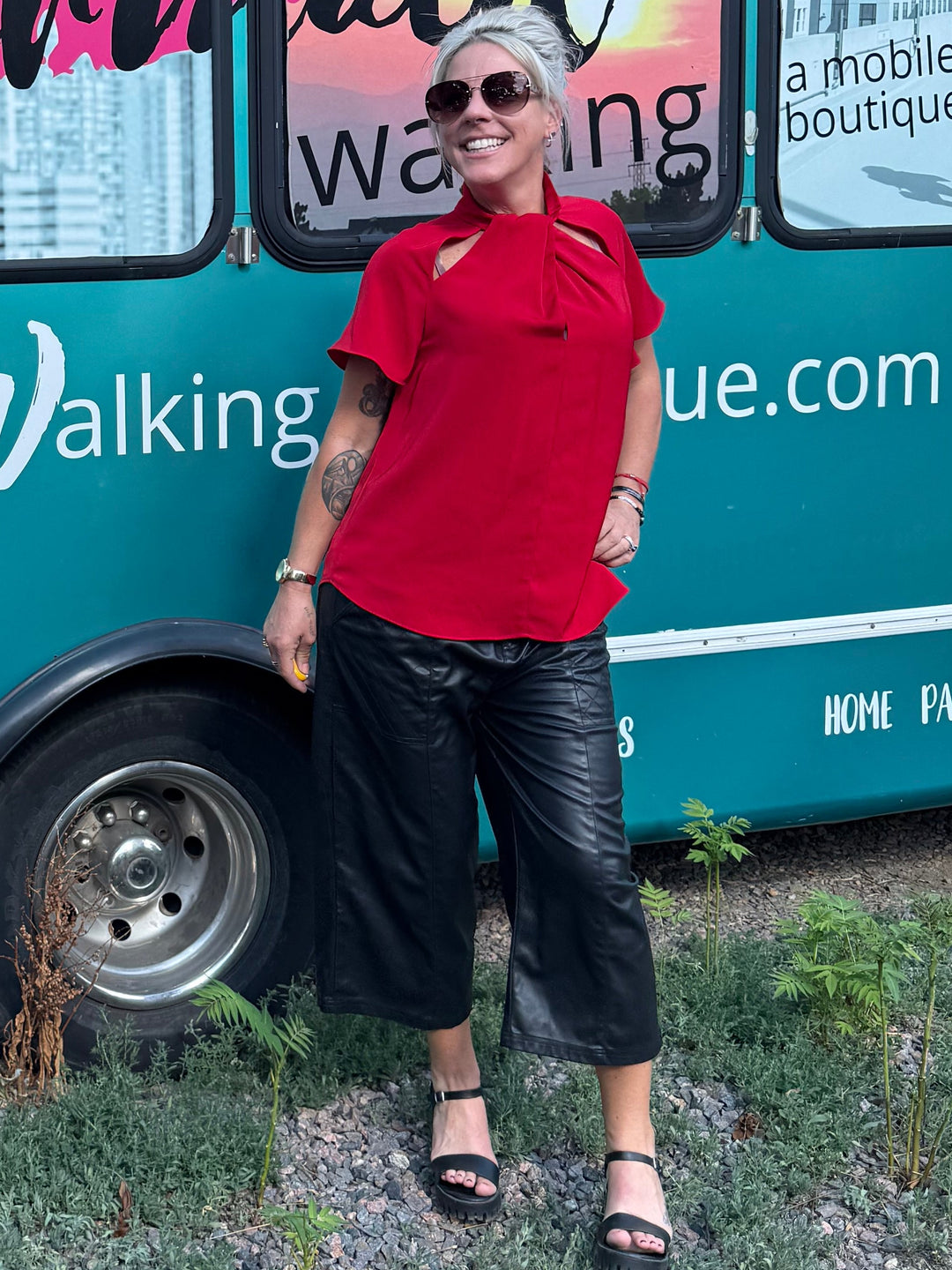 A woman in a red shirt and black pants stands next to a teal bus with &
