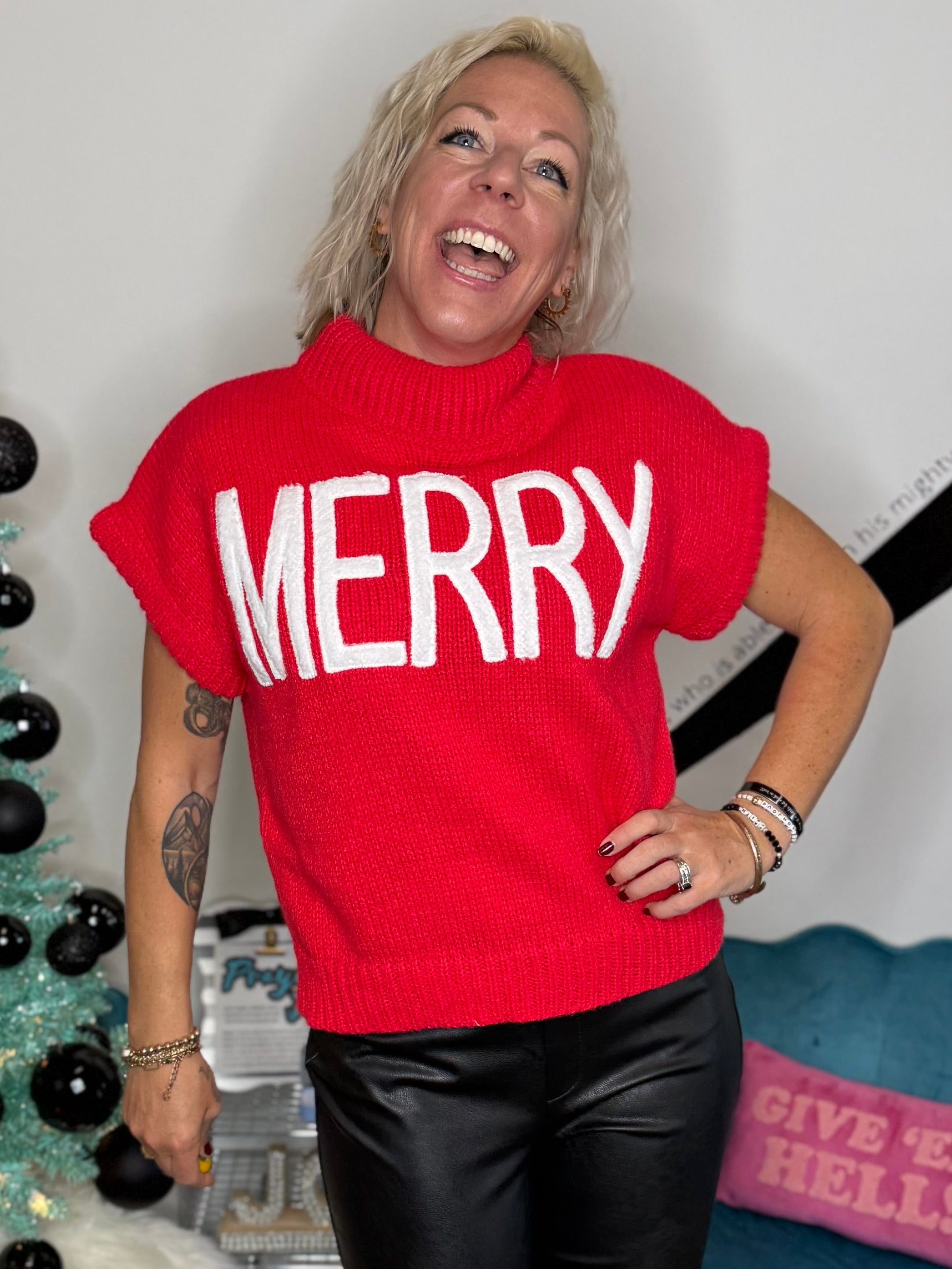Person wearing a red 'MERRY' shirt standing in front of a decorated Christmas tree.