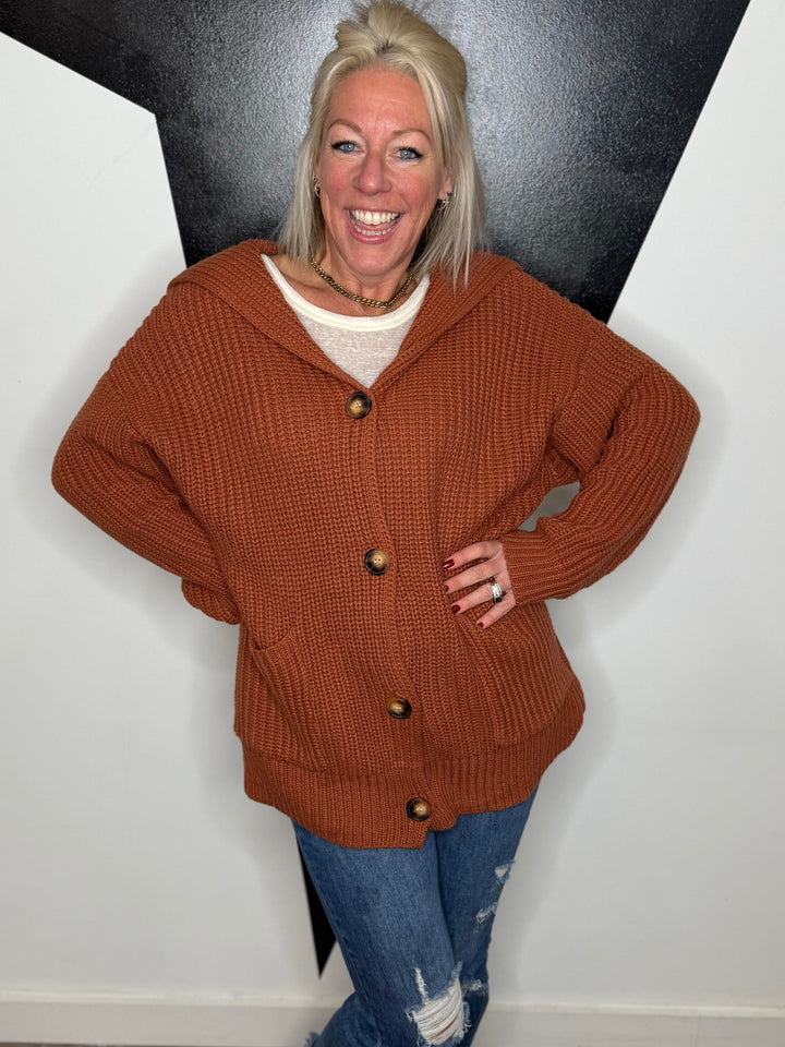 Woman wearing a brown cardigan with a black and white geometric wall background