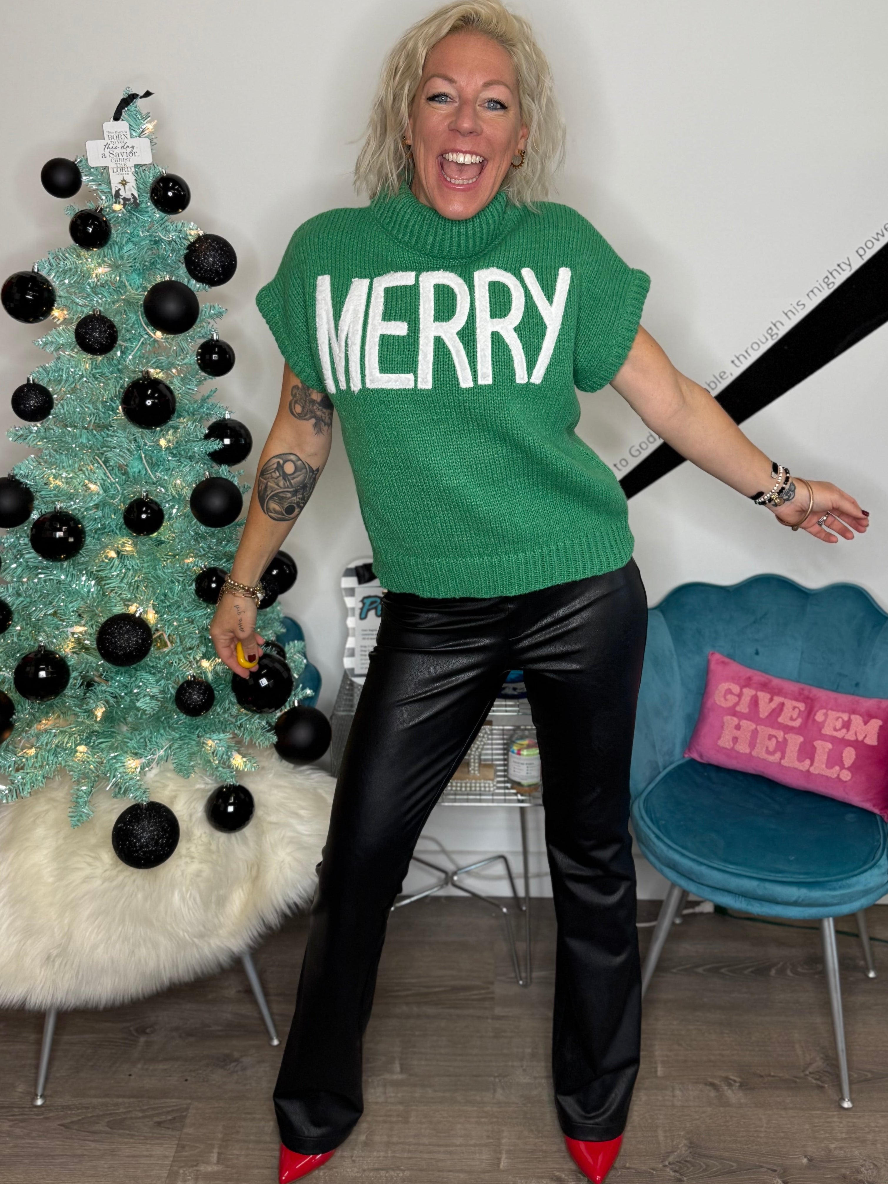 Person wearing a green 'MERRY' shirt in front of a decorated Christmas tree.