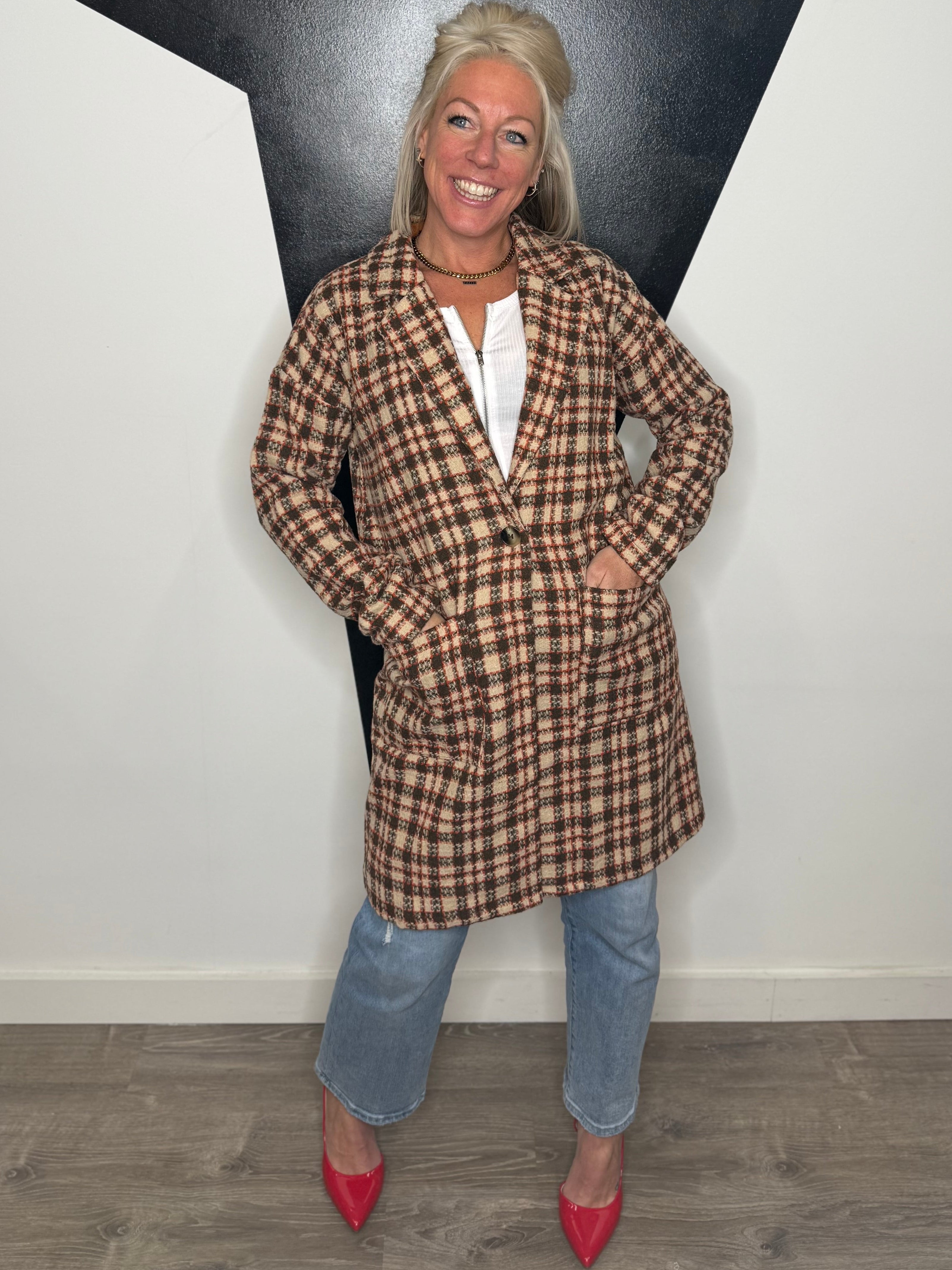 Woman wearing a plaid coat and jeans standing against a plain wall.