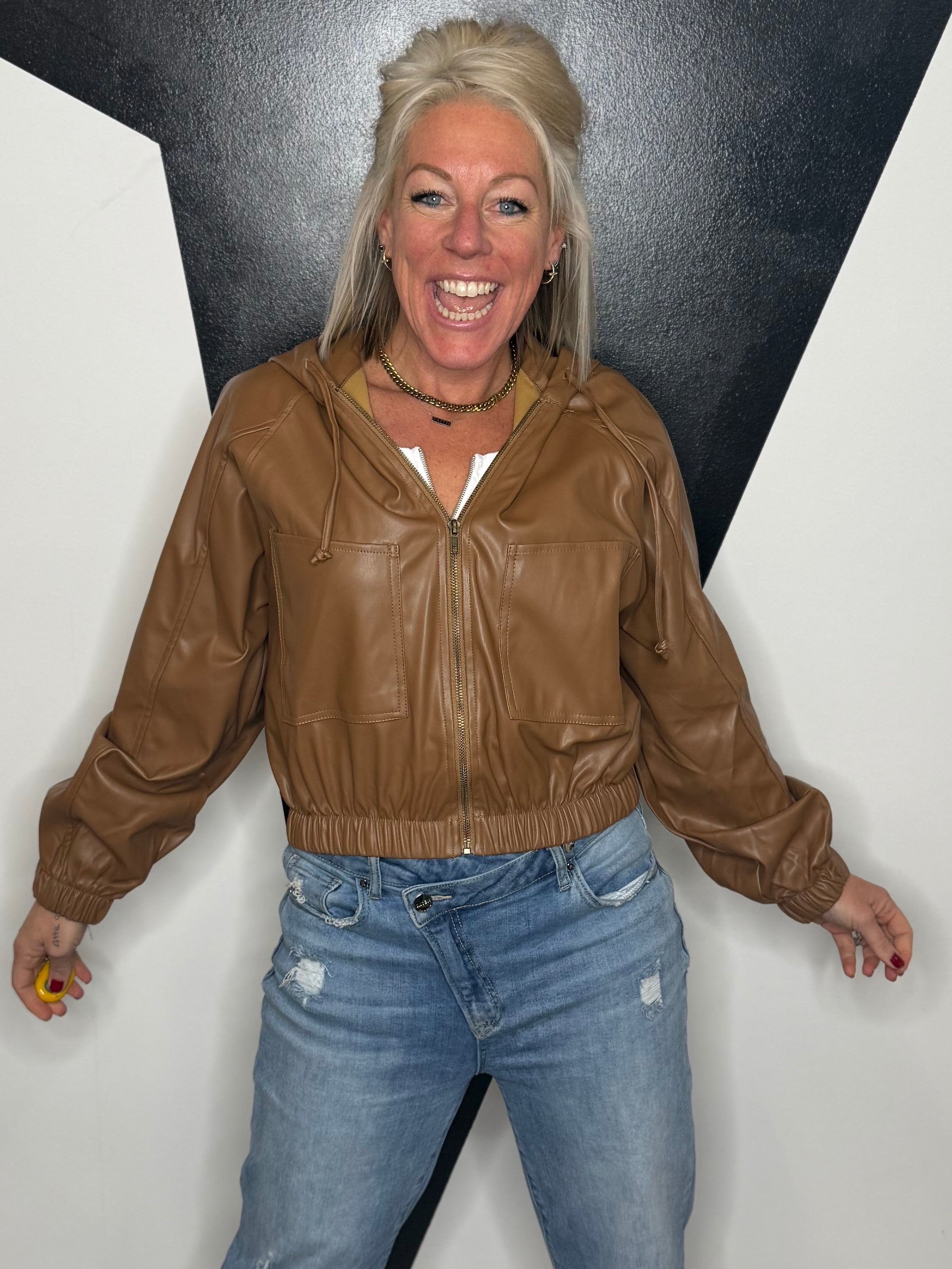 Person wearing a brown leather jacket and blue jeans against a plain background