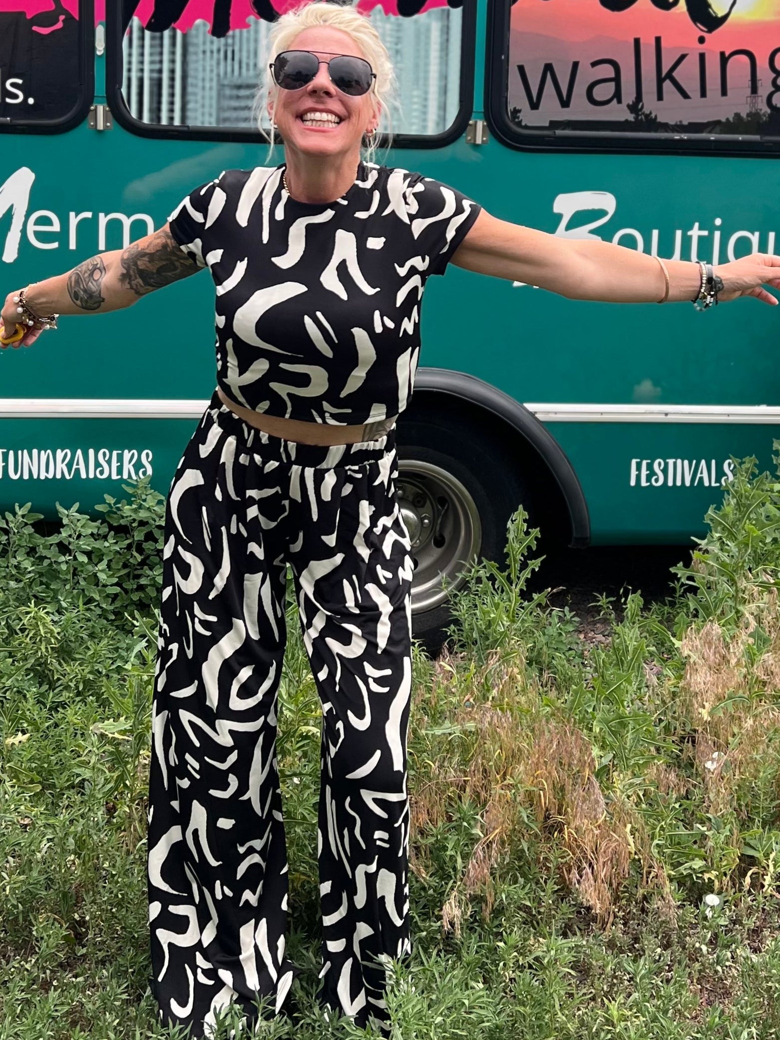 Person in a patterned outfit standing in front of a mobile boutique bus with 'Mermaid Walking' branding.