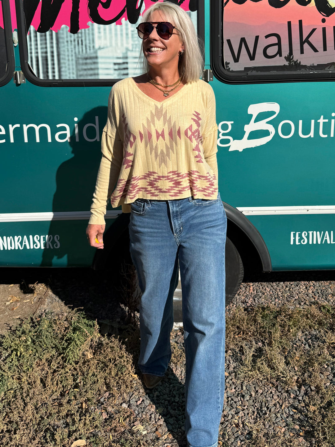 A woman with blonde hair and sunglasses stands smiling in front of a teal bus with &