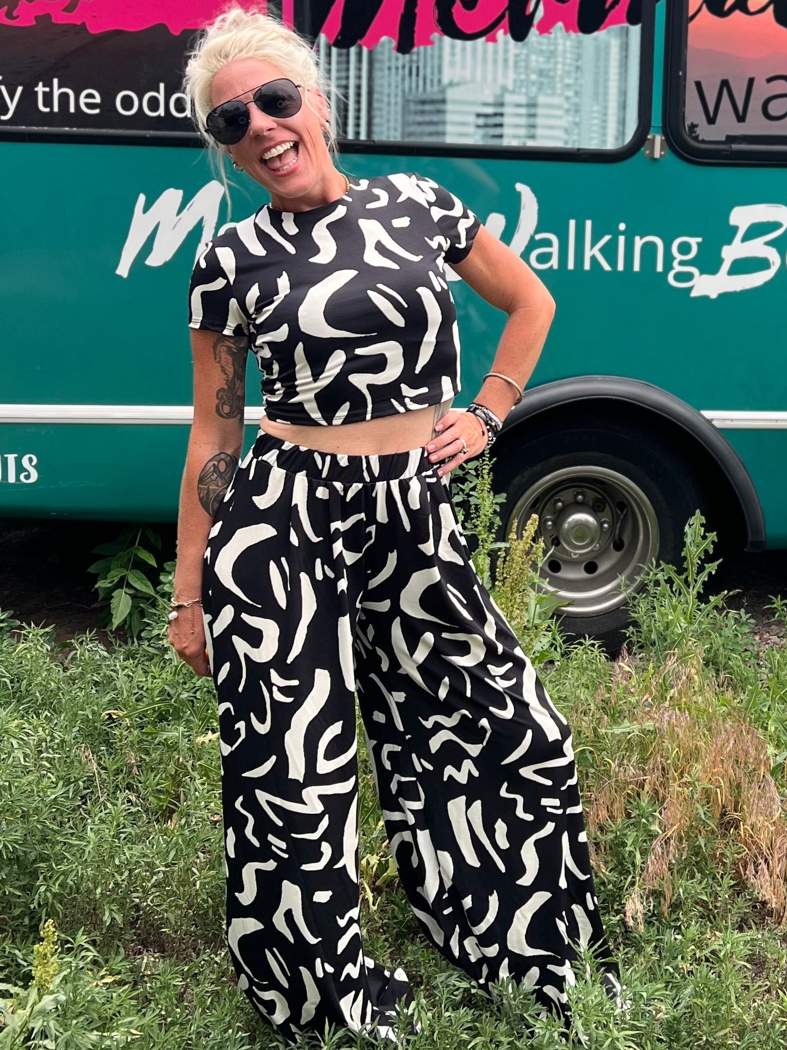 Woman in a black and white patterned outfit standing in front of a teal bus with 'Mermaid Walking' branding.