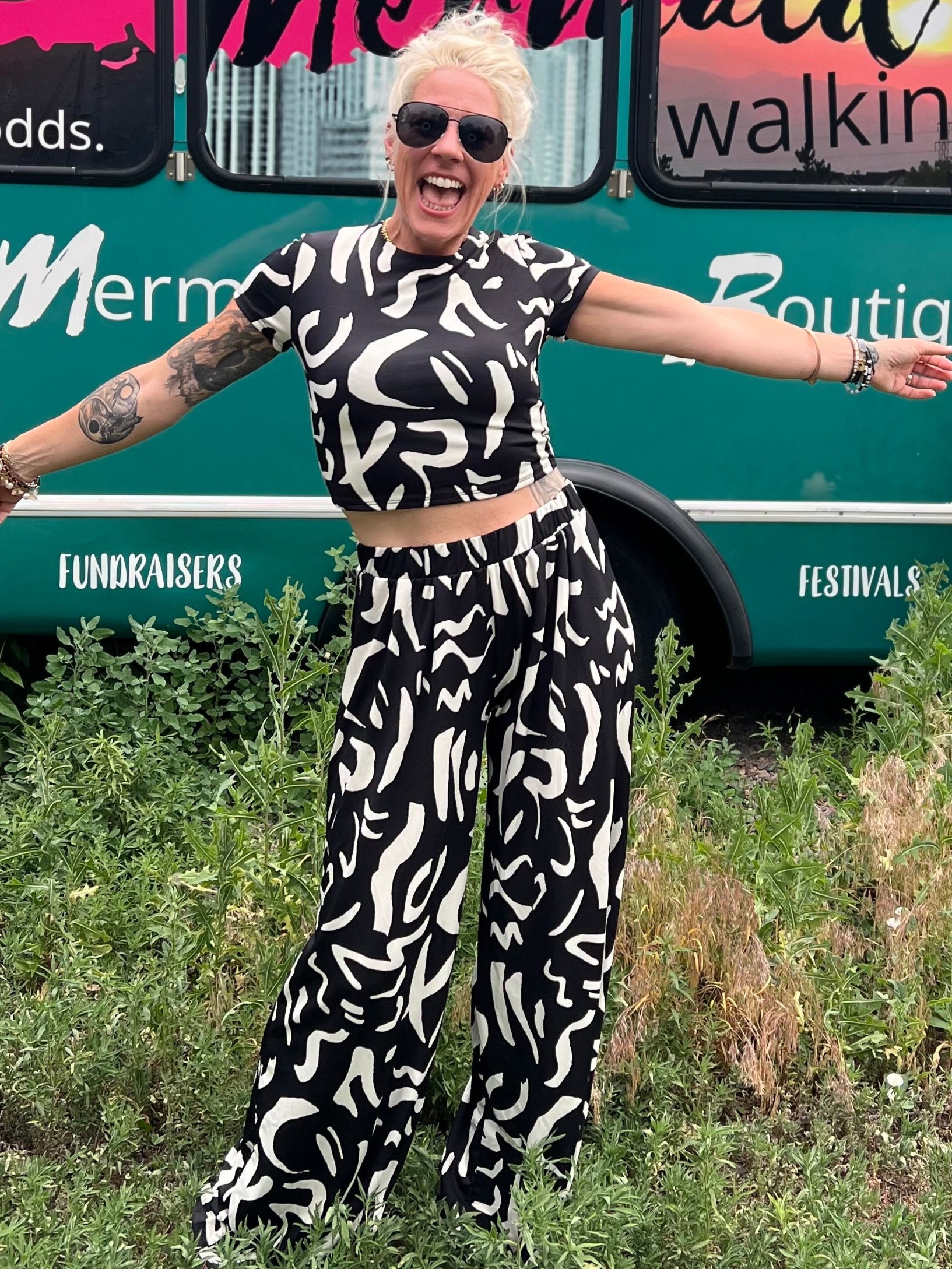 Person in a black and white patterned outfit standing in front of a mobile boutique bus.