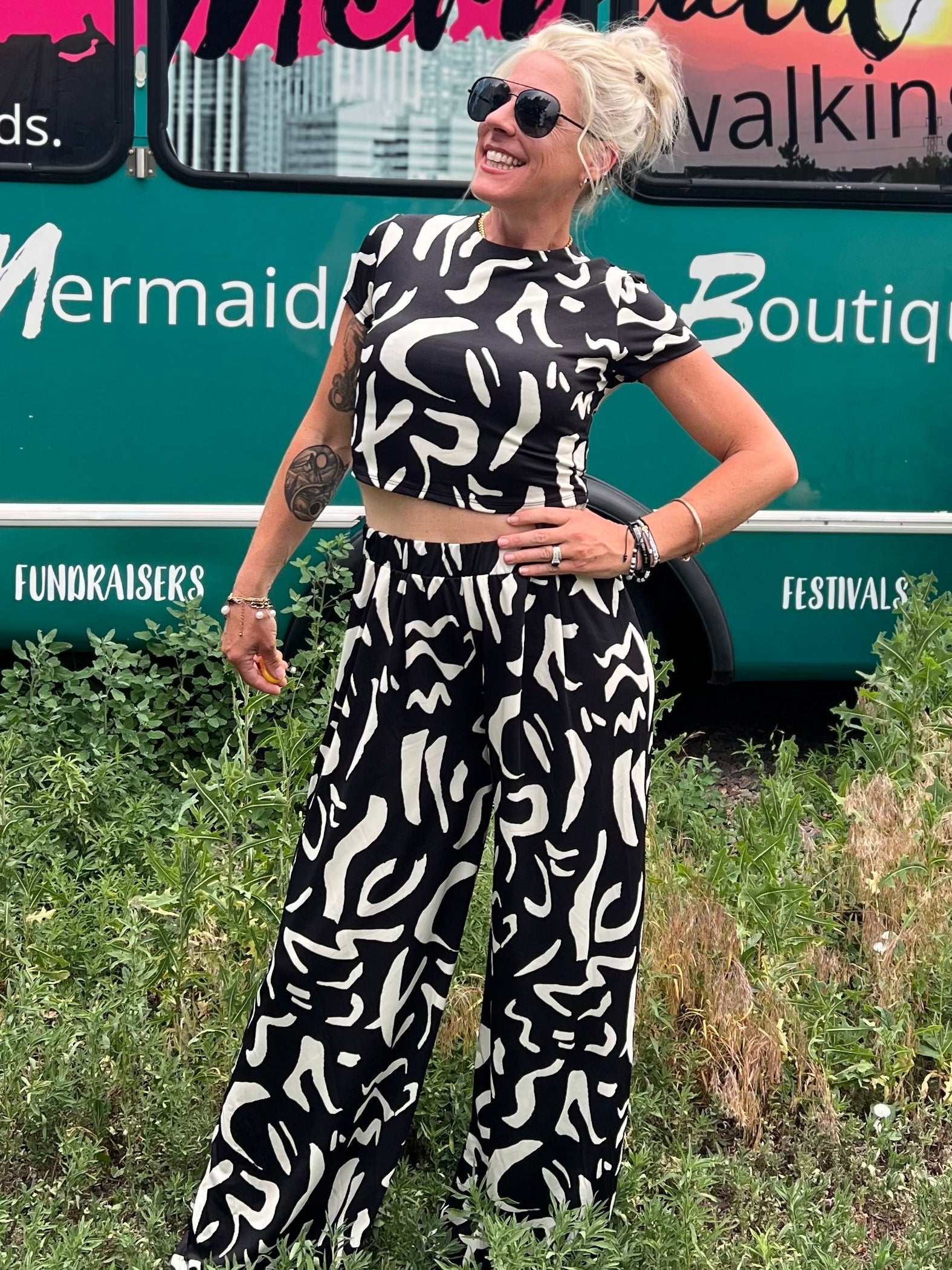 Woman in a black and white patterned outfit standing in front of a mobile boutique bus.