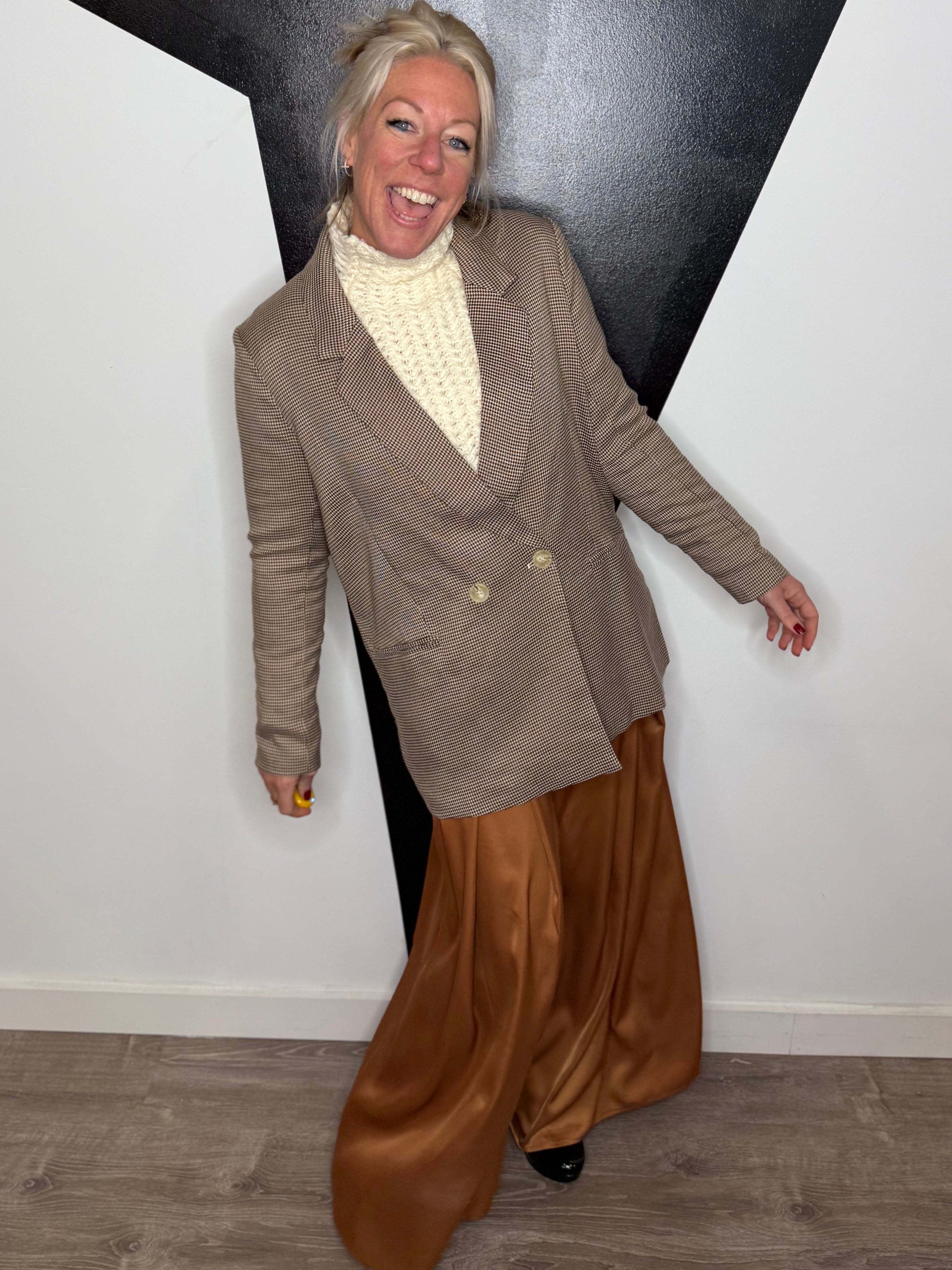 Person wearing a brown blazer and wide-leg pants standing against a black and white geometric wall.